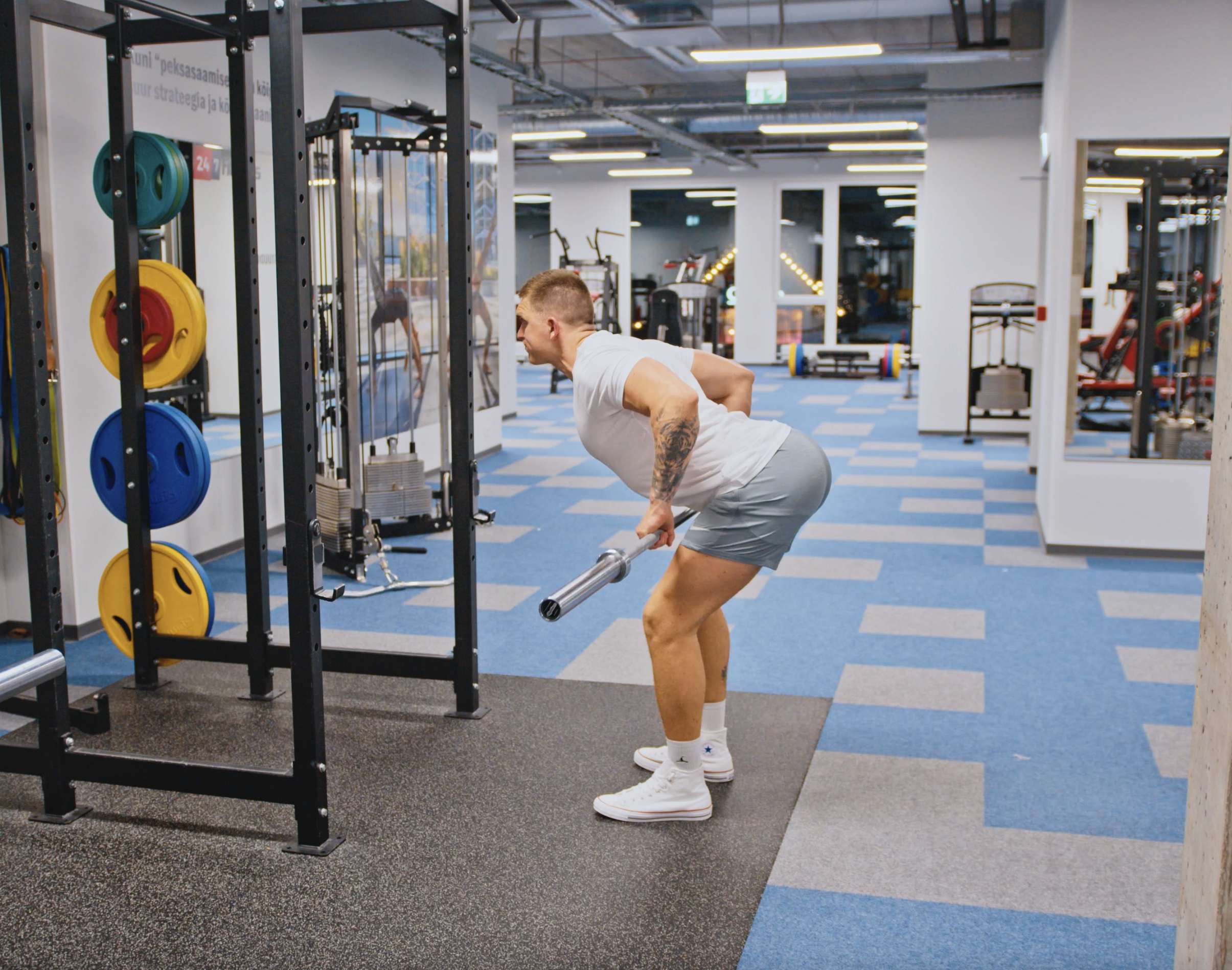 personal trainer performing bent over barbell row in 24-7 fitness gym
