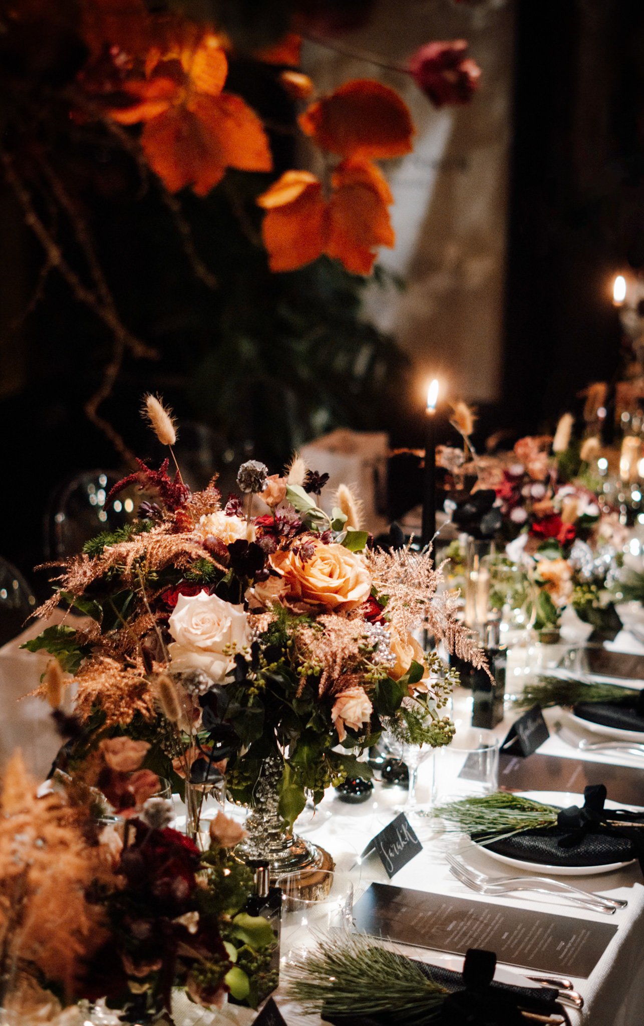 A table decorated with floral arrangements, candles, and place settings in a dimly lit setting.