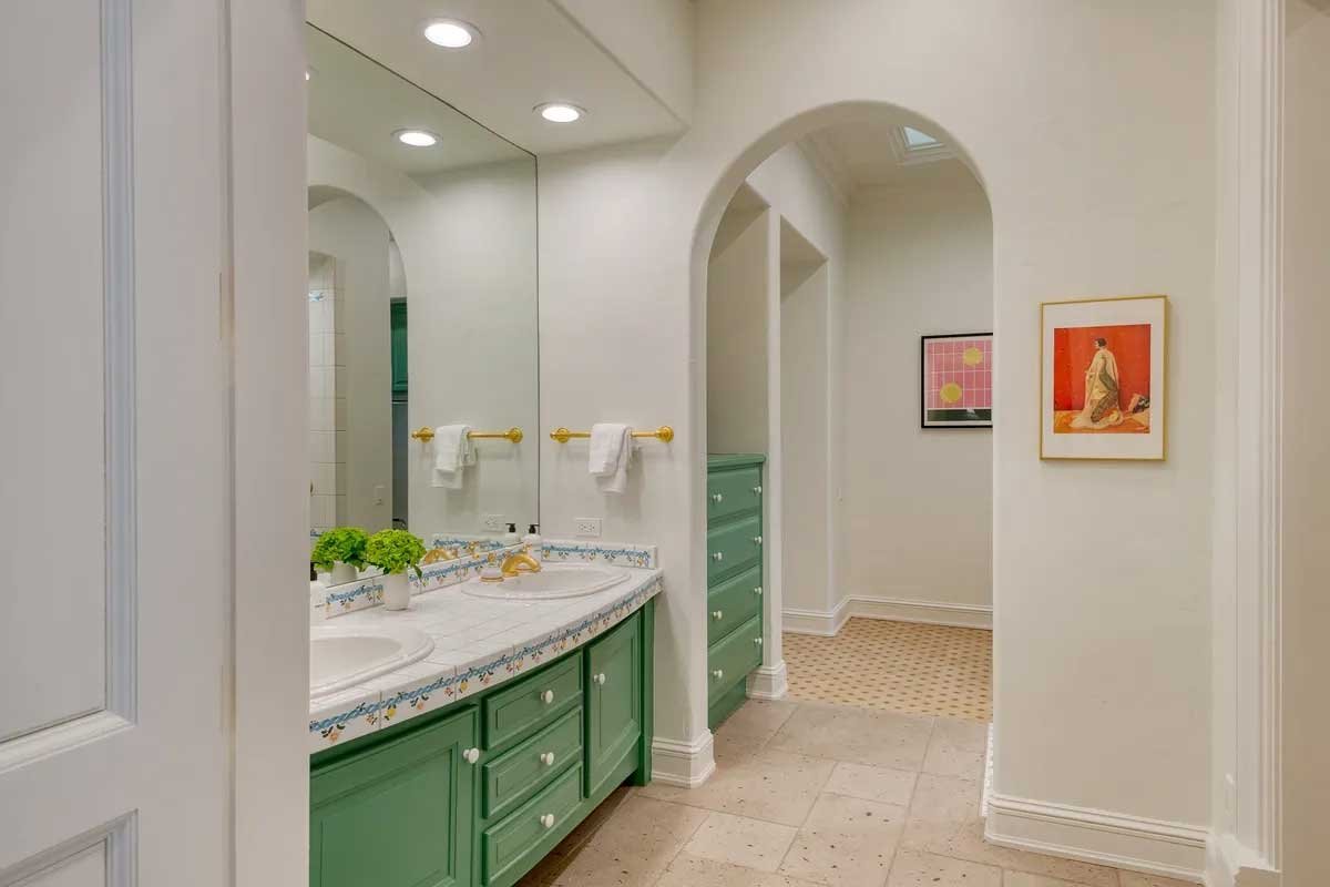 Elegant bathroom with green cabinetry, a large mirror, and decorative tiles around the sink. Two framed artworks are mounted on the walls, and there are recessed ceiling lights. Towels are hanging on gold-tone bars.