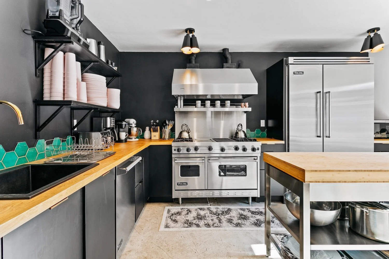 Modern kitchen with black cabinets, stainless steel appliances, and teal hexagon backsplash tiles.
