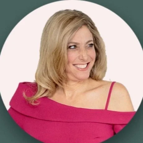 Smiling woman with blonde hair wearing a pink off-shoulder top against a white background.