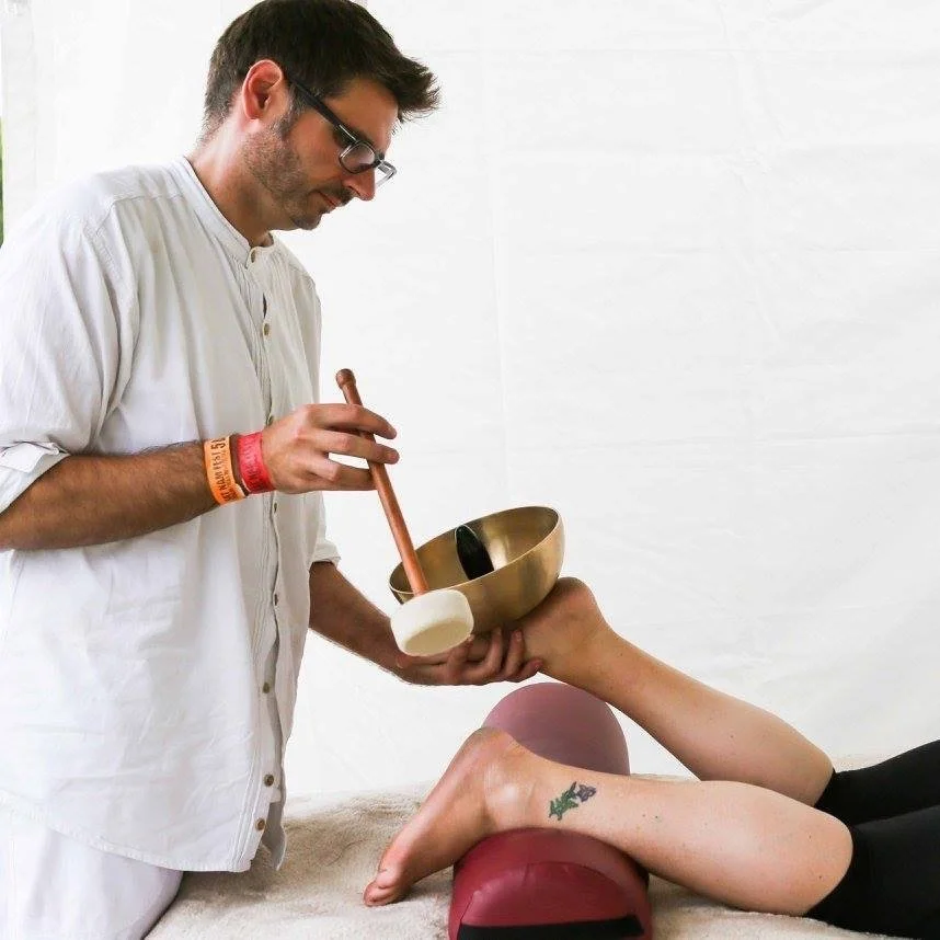 Man using a Tibetan singing bowl near a person's feet during a sound therapy session.