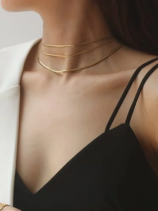 Mujer con collar de oro y vestido negro con tirantes finos.