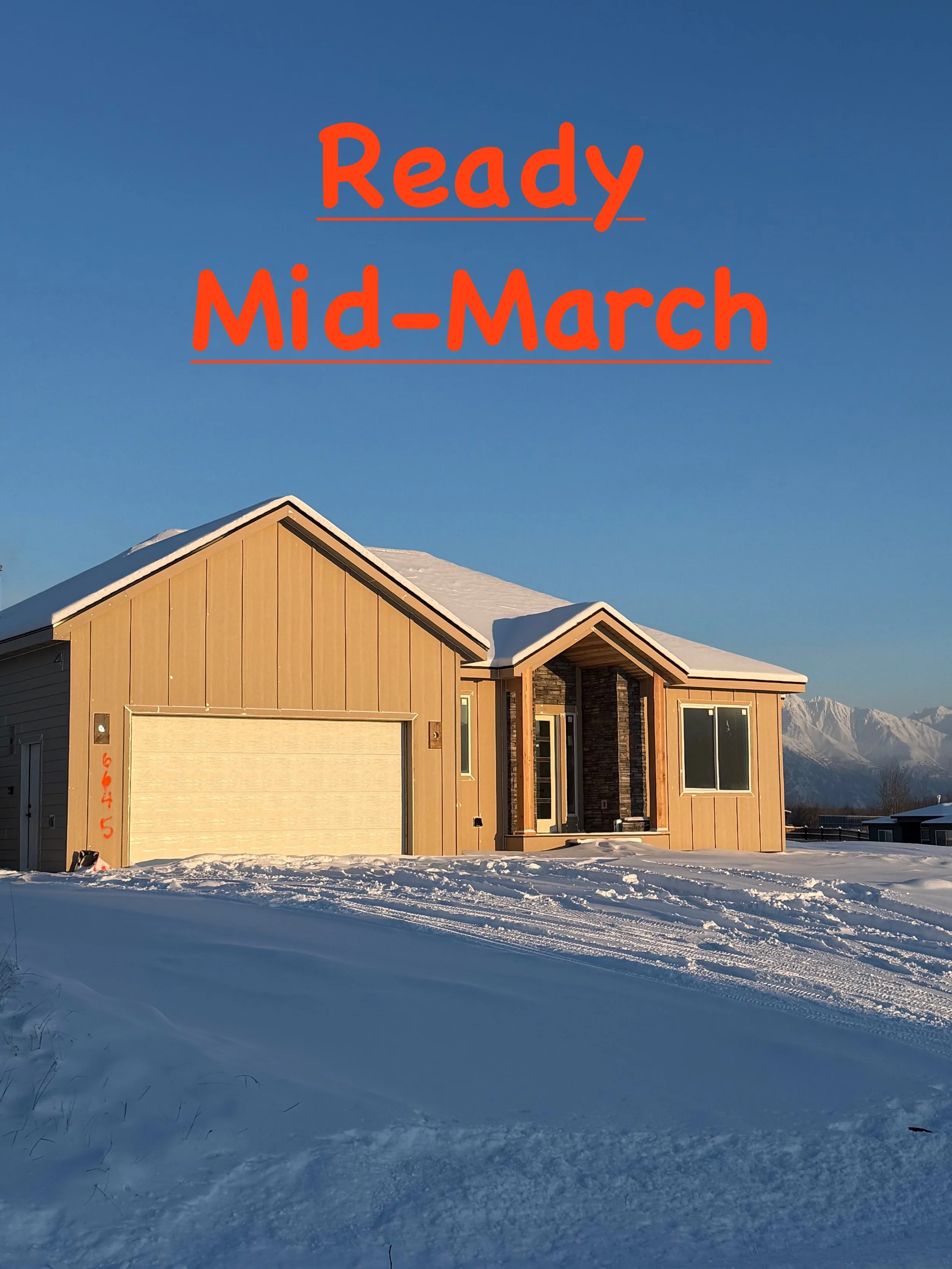 A house under construction with wooden framing and green building wrap, set against a clear blue sky, on a dirt lot.