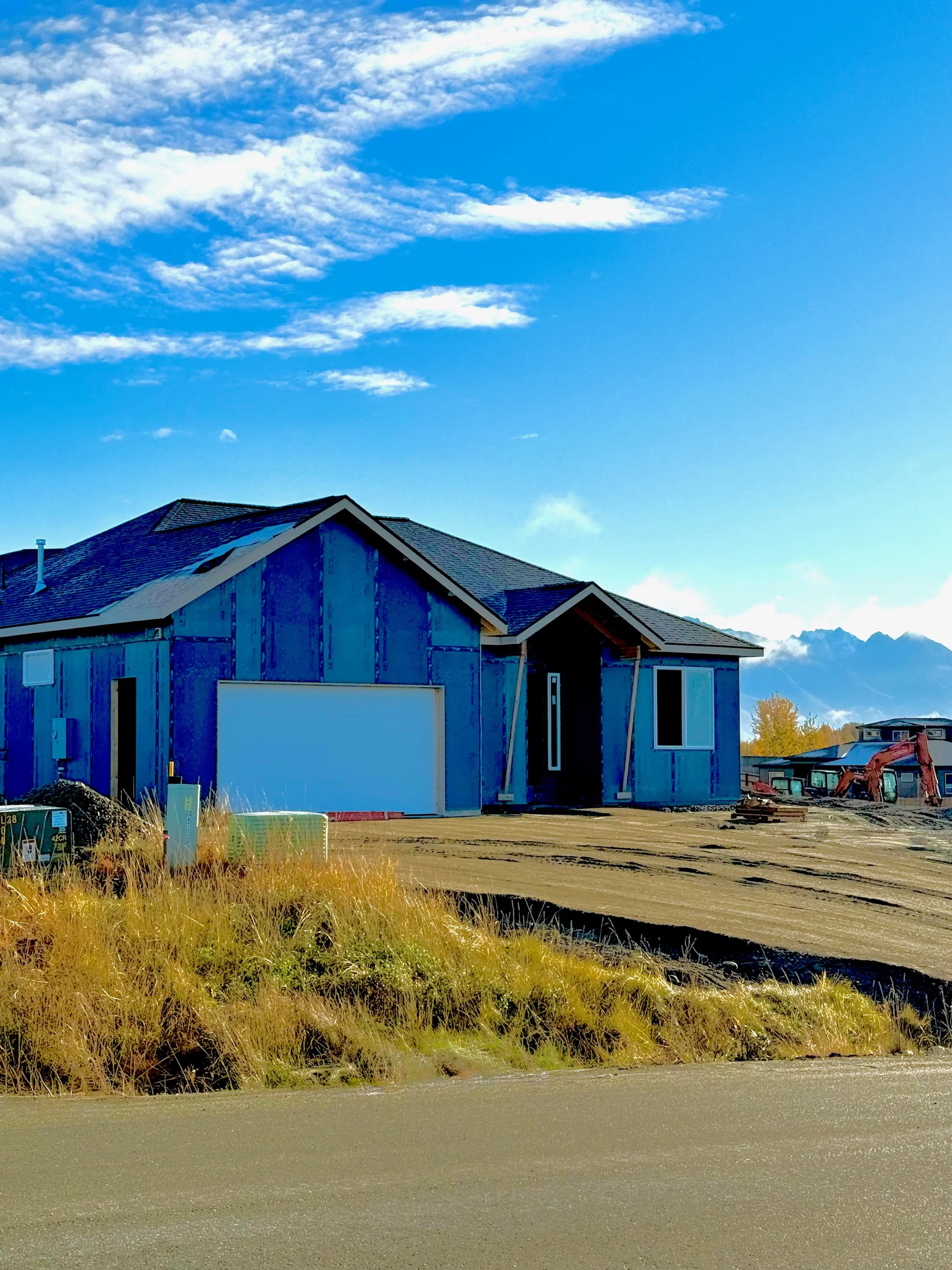 New house under construction in a suburban area, with a blue sky and mountains in the background.