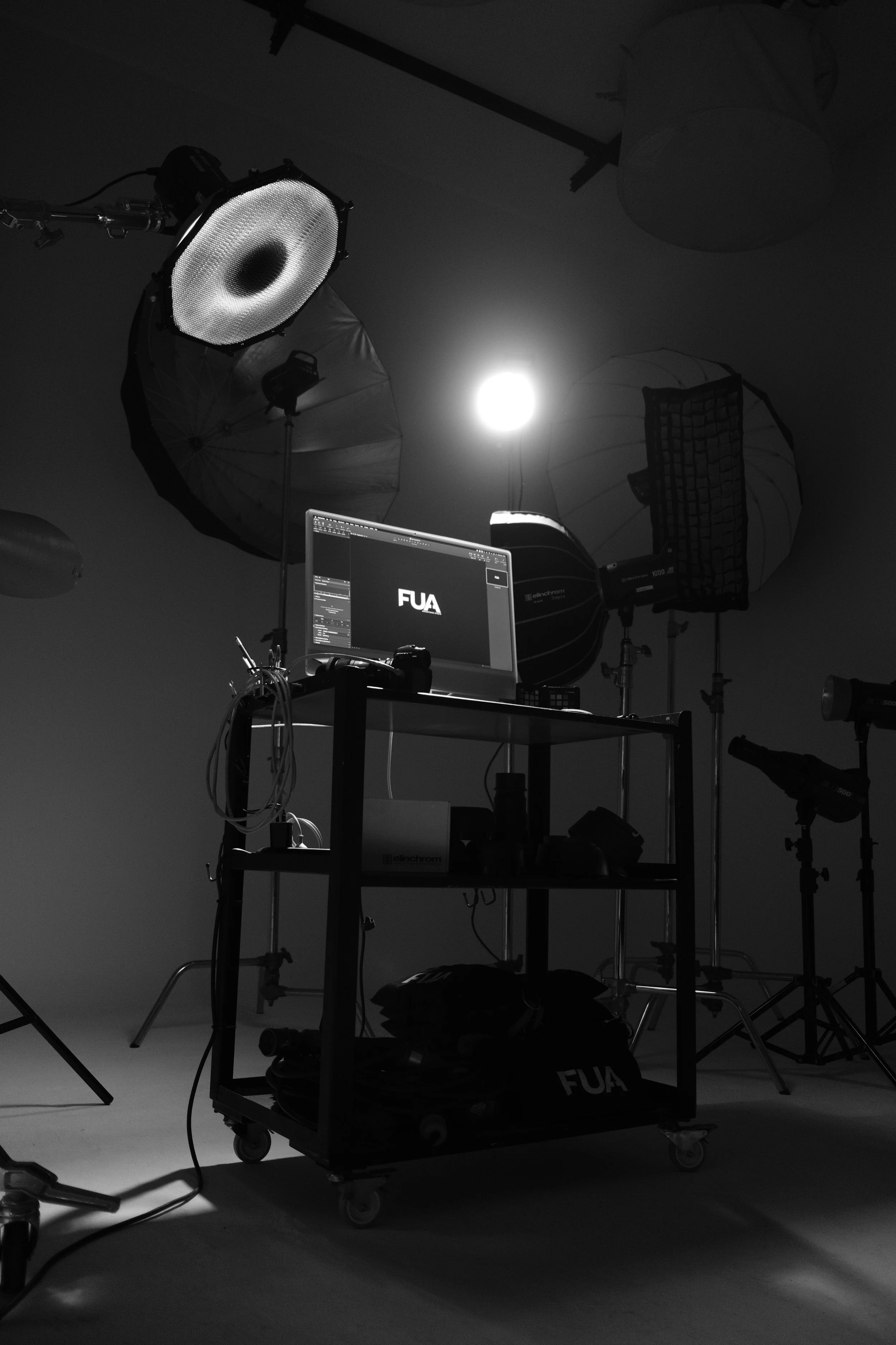 Photography studio setup with professional lighting equipment and a computer displaying the logo 'FUA', against a plain background.