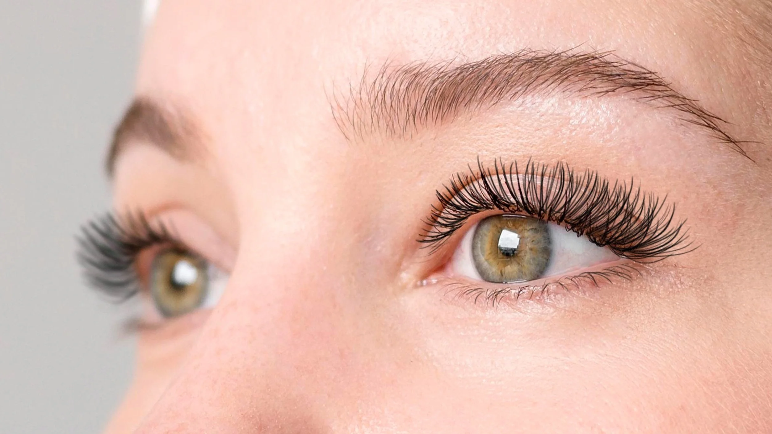 Close-up of a person's blue-green eye with long eyelashes and well-groomed eyebrows.