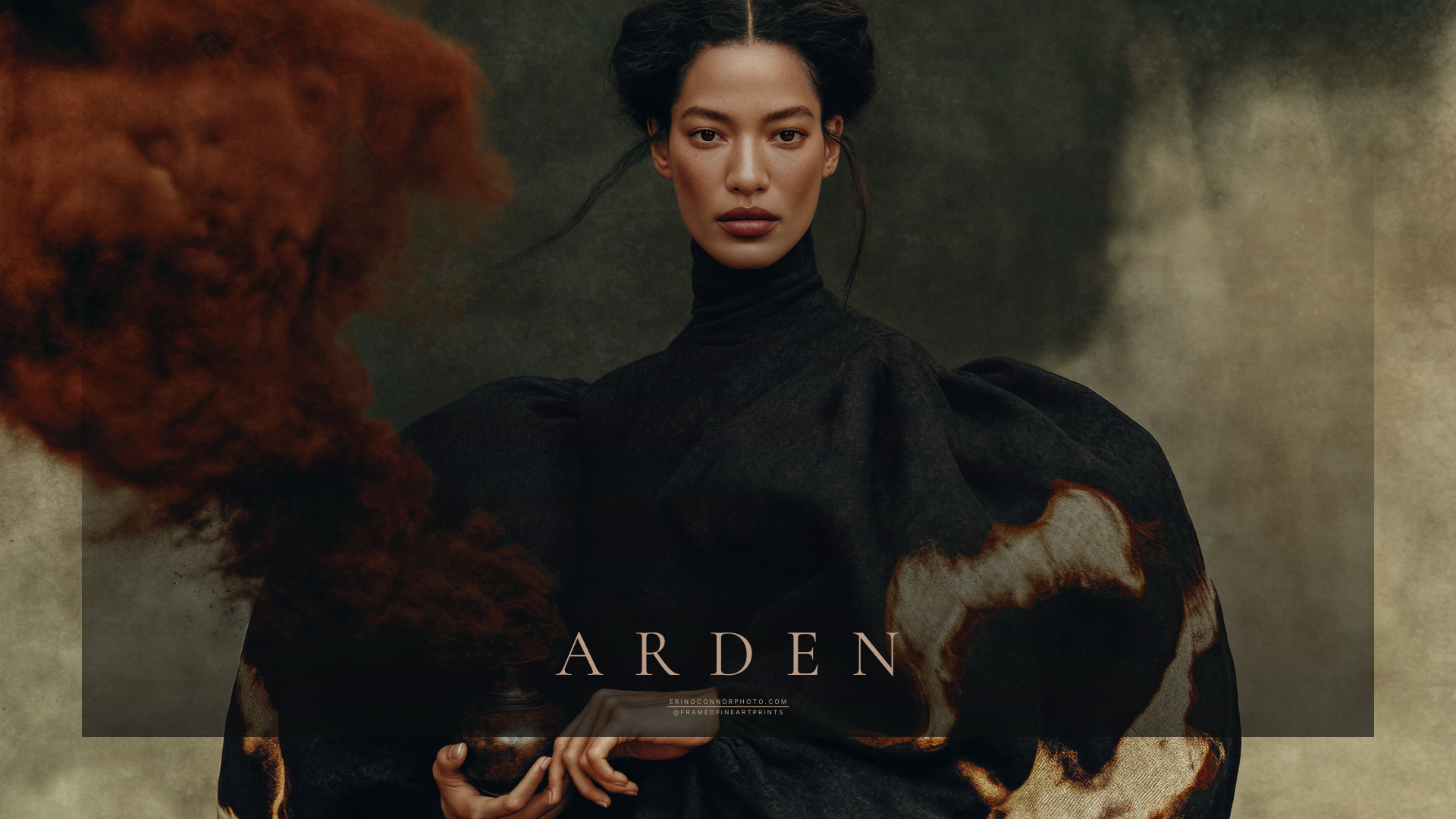Arden holding a small dark vessel as a rust colored plume rises beside her black sculptural garment.