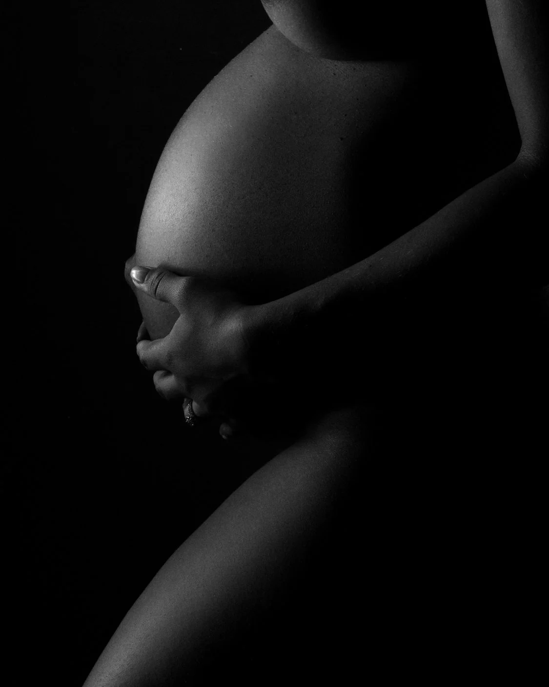 Black-and-white close-up maternity portrait of hands gently resting around a pregnant belly.
