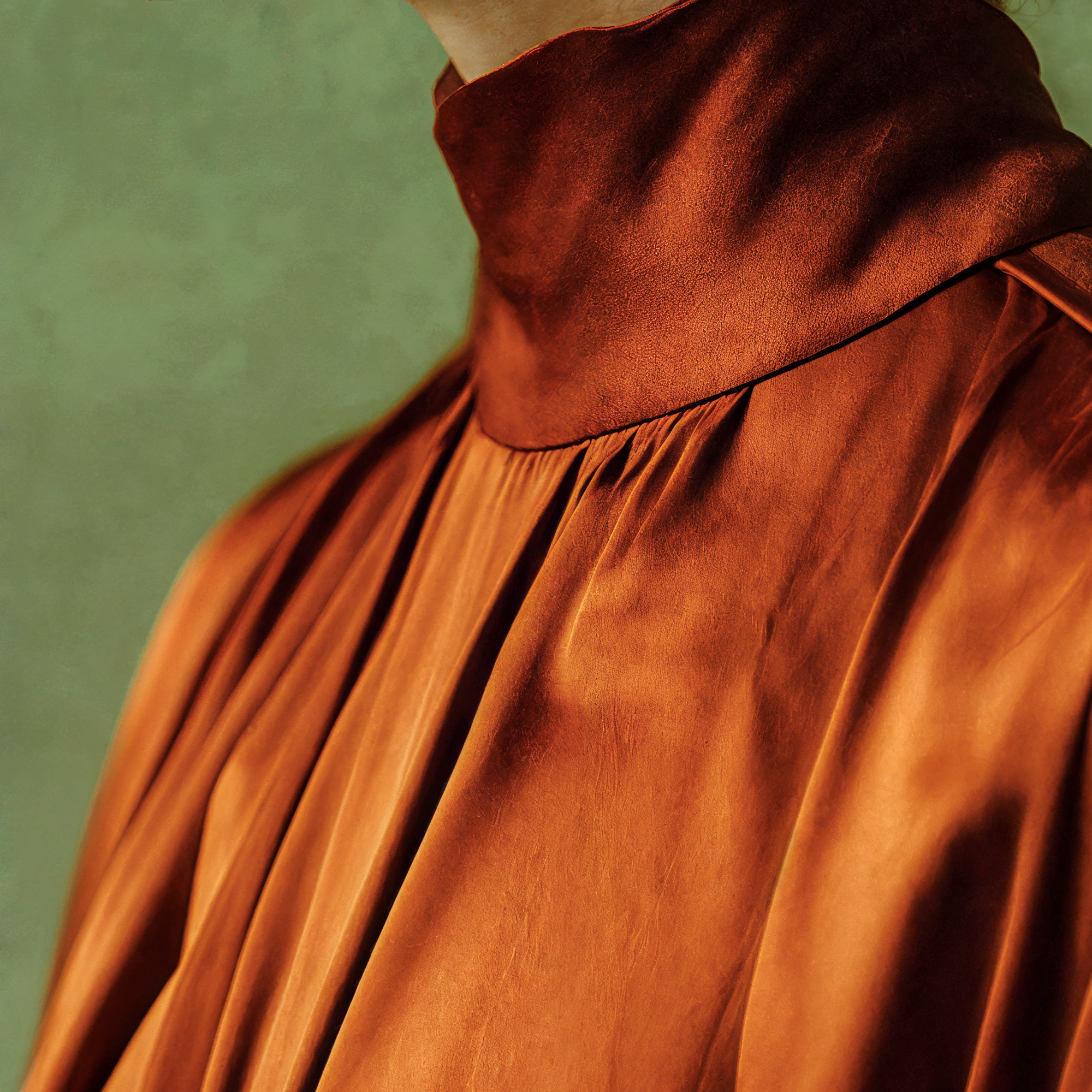Close detail of the gathered collar and deep folds of Rowan's burnished rust-colored garment.