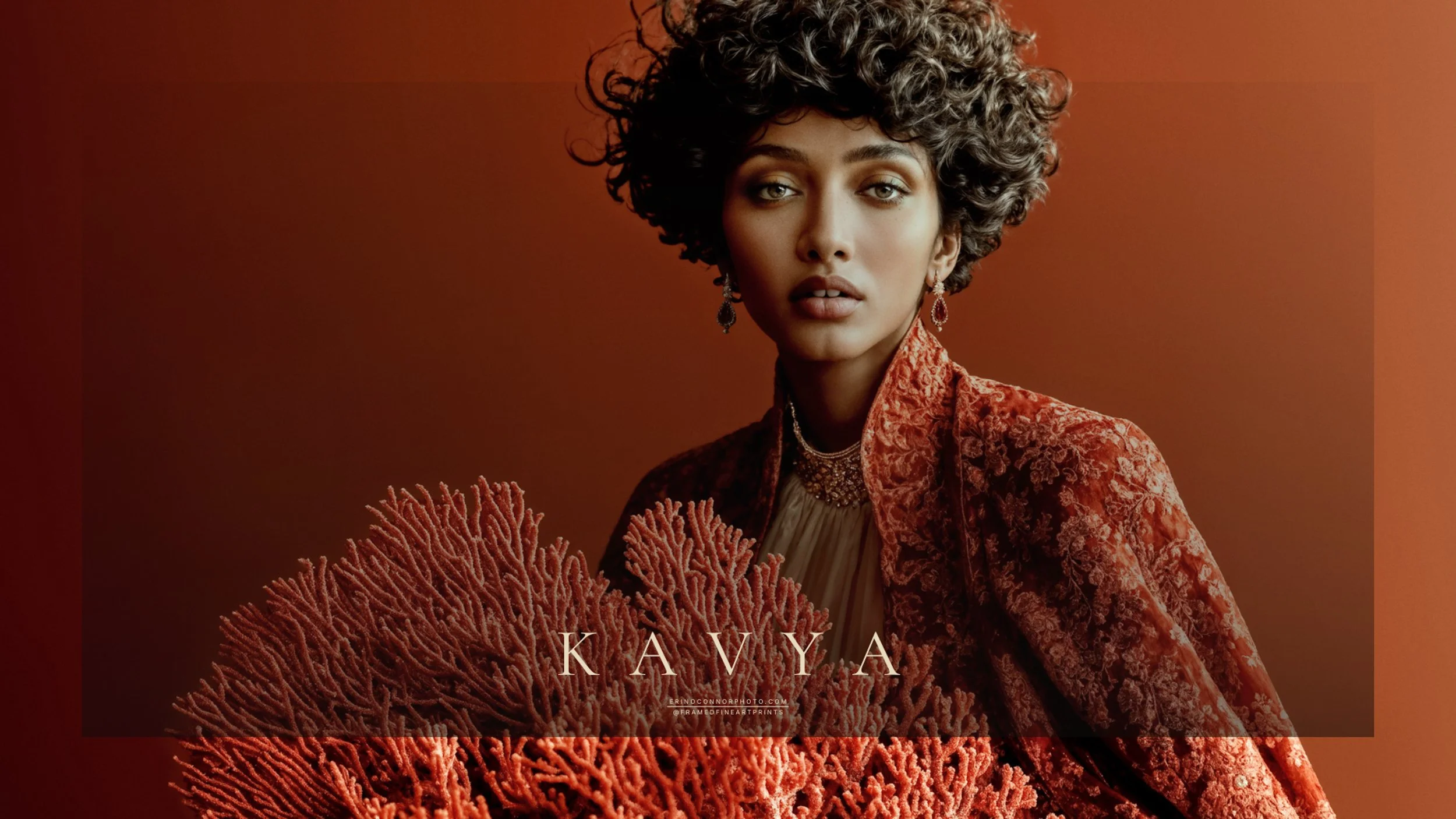 Kavya beside a large branching red coral formation, wearing richly textured red clothing against a warm terracotta background.