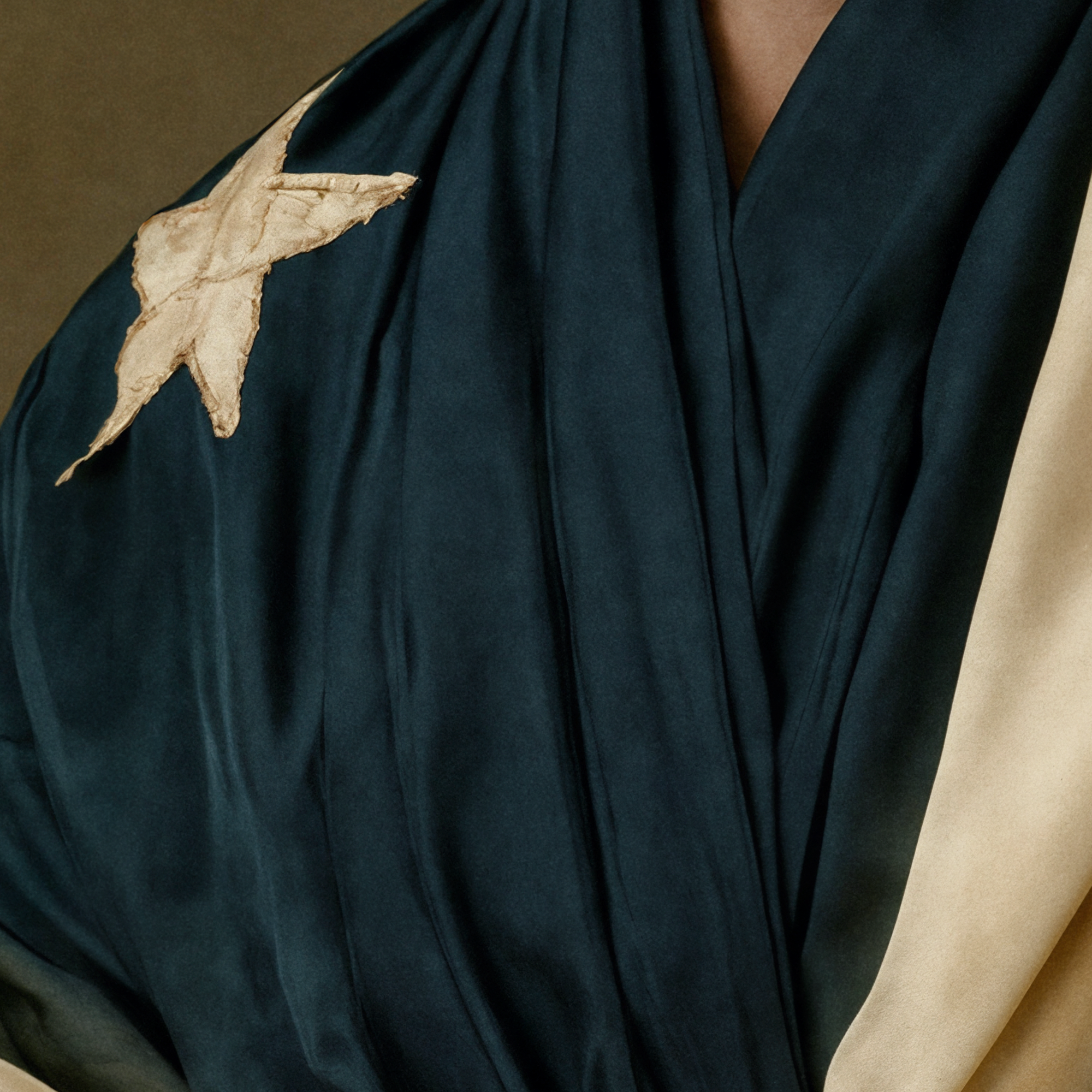 Close detail of a pale unidentified emblem set against the dark blue fabric of Simone’s garment.