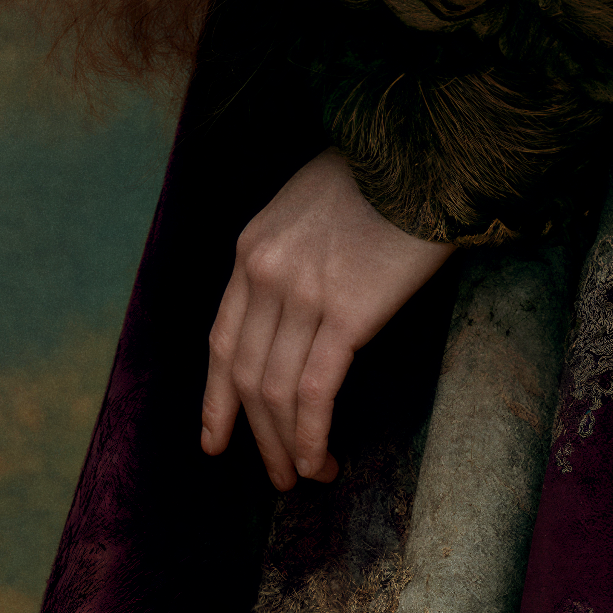 Close detail of Cressida's hand emerging from the folds of her monumental floral brocade garment.