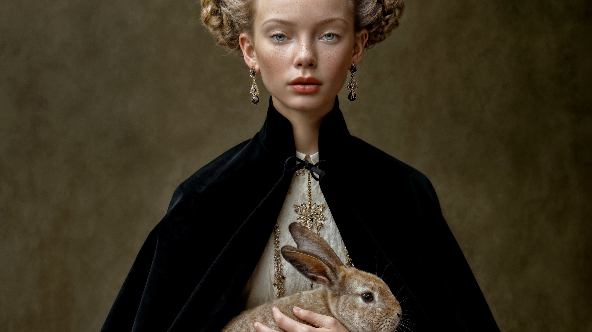 Eira wearing a black velvet mantle and embroidered ivory gown while gently holding a brown rabbit.