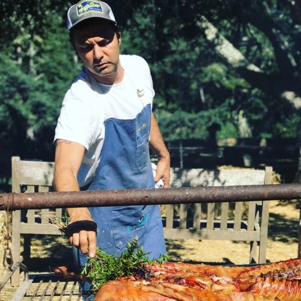 Chef grilling meat and seafood over open fire for a Colectivo Felix Asado Argentino