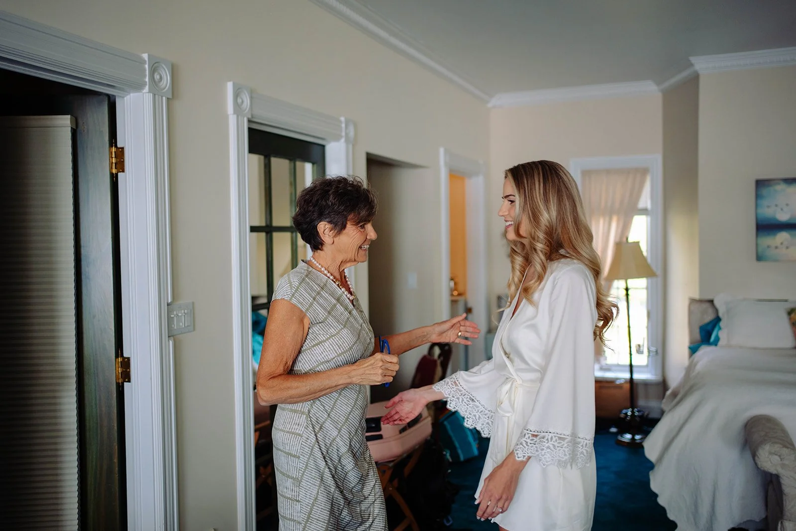 Two women, an elderly woman and a young woman, are smiling and talking inside a bedroom.