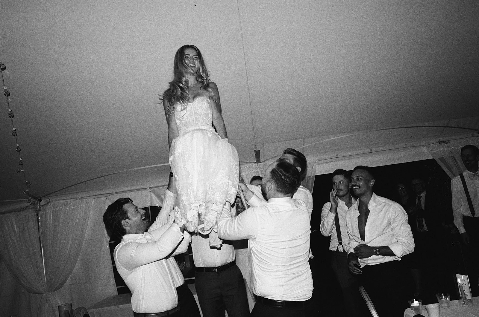 A group of men lifting a woman in a wedding dress during a celebration or wedding reception.