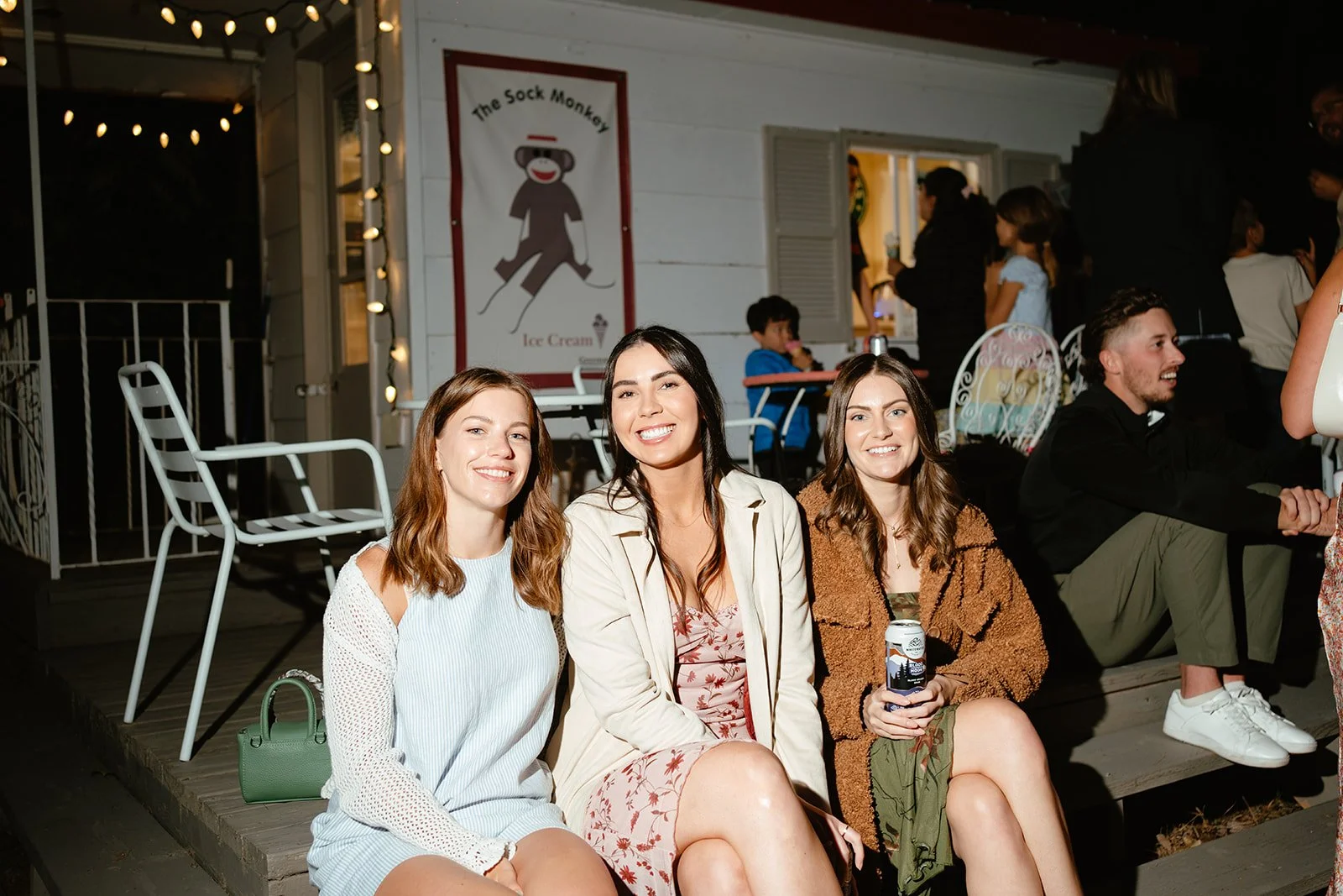 Group of young women sitting outdoors at night, smiling, with a sign for 'The Sock Monkey' ice cream shop in the background.