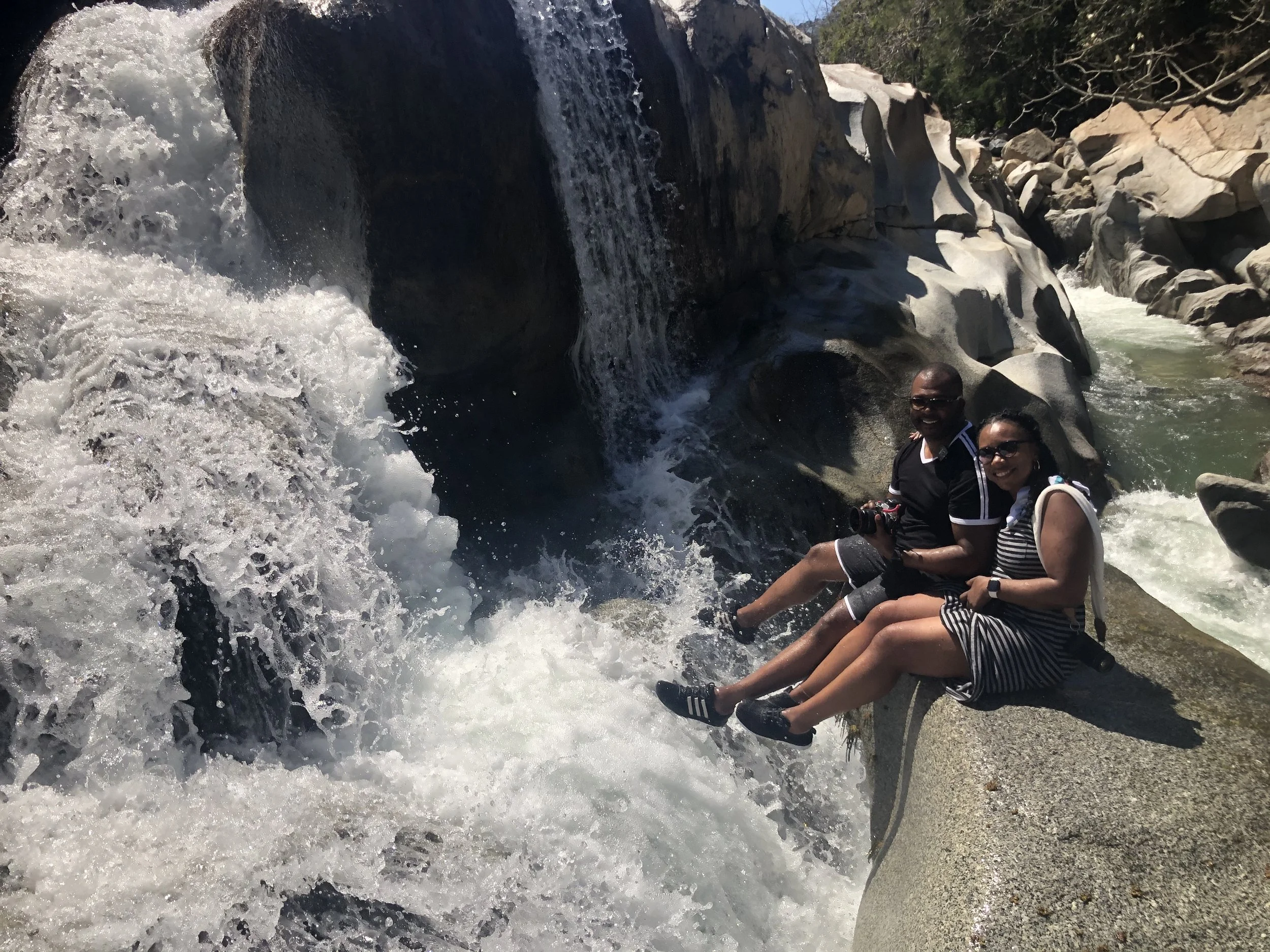 Addy and Terry standing in shallow water beneath a waterfall in Puerto Vallarta.