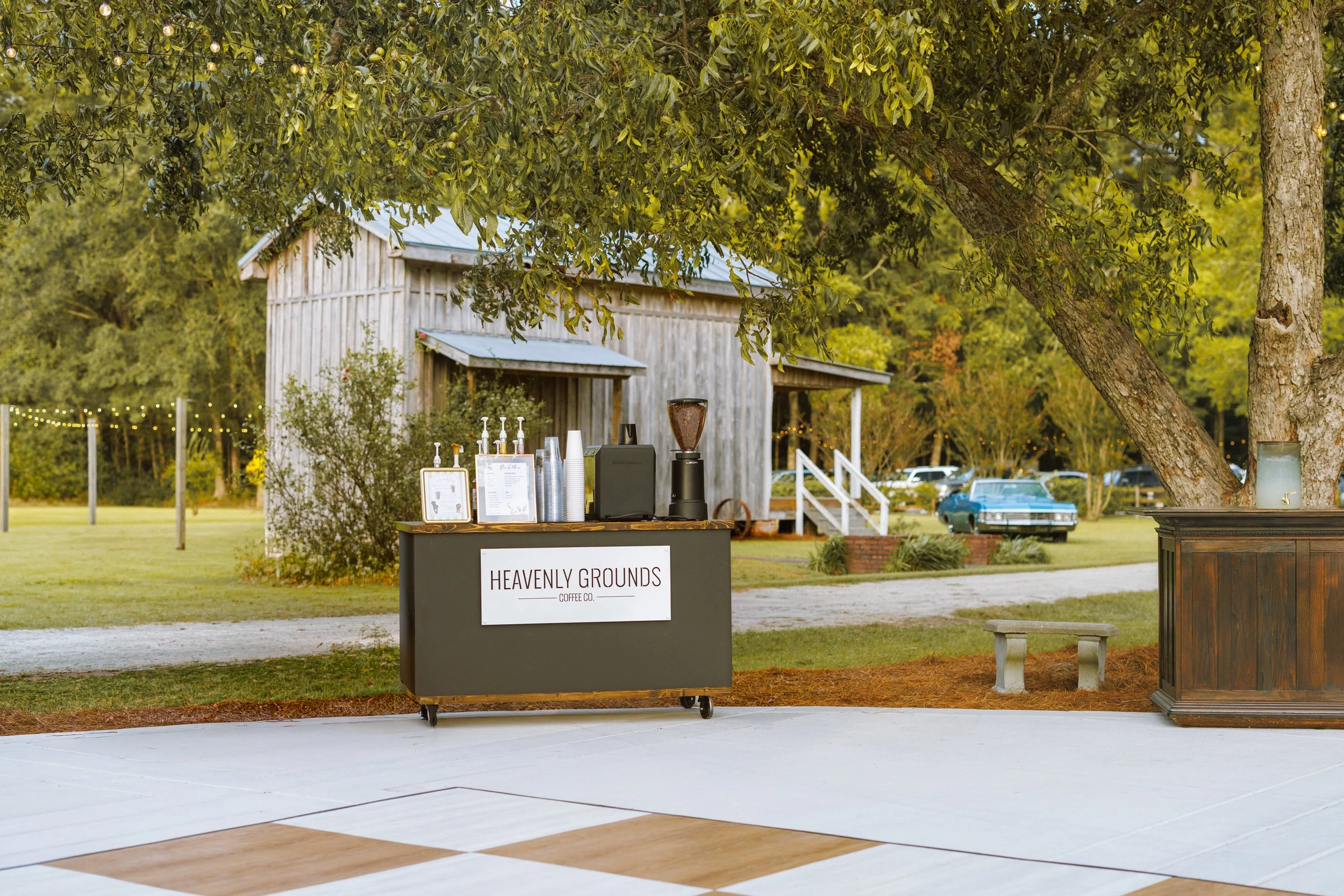 A black coffee cart with wood serving top and white Heavenly Grounds Coffee Co metal sign on the front at a wedding venue