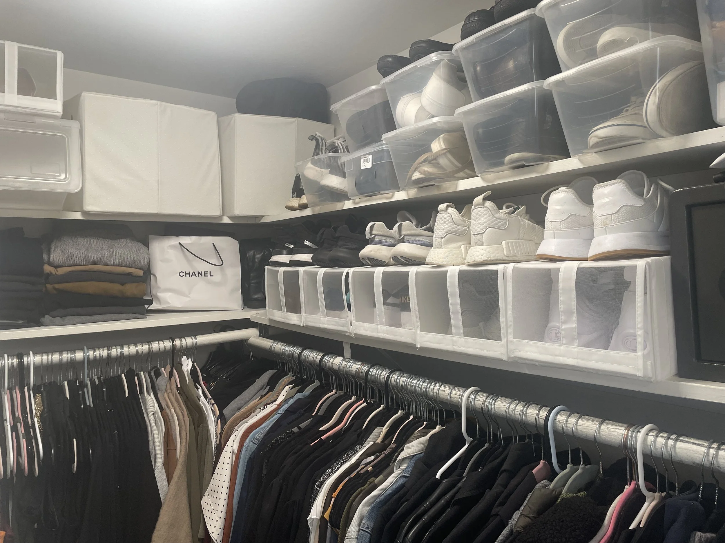 Closet with shelves containing shoe boxes and sneakers, alongside a clothing rack with variously colored clothes.