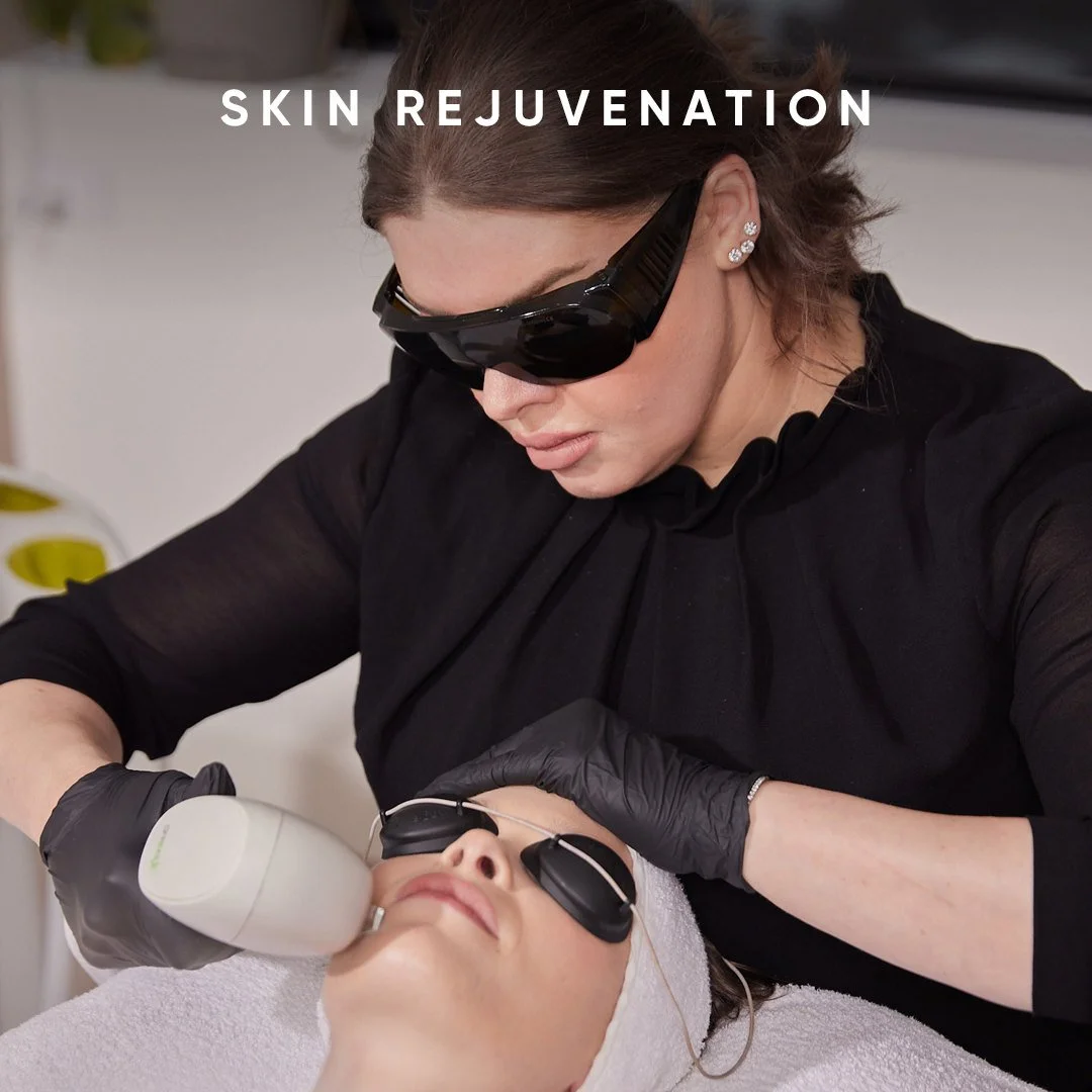 A woman receiving a skin rejuvenation treatment with a handheld device from a technician wearing black gloves, black attire, and protective eyeglasses, in a spa or clinic setting.