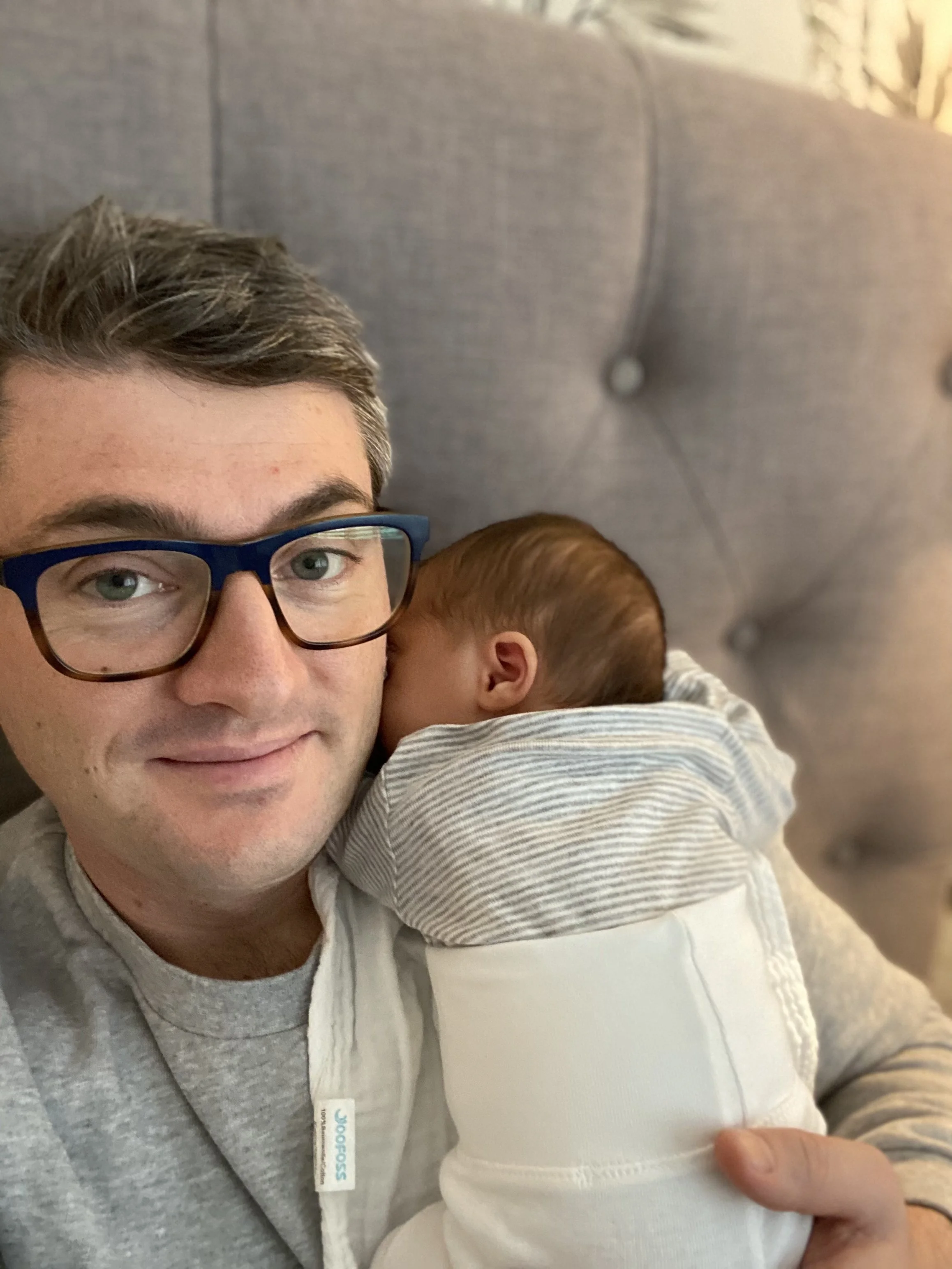 A man with glasses holding a newborn baby snuggled up to his face.