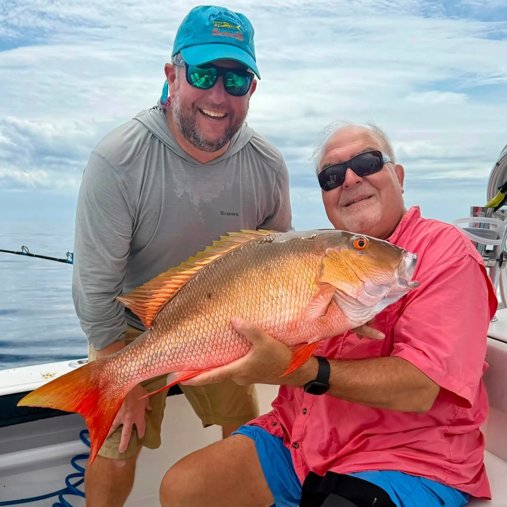 Two smiling men on a boat holding large snapper in the ocean.