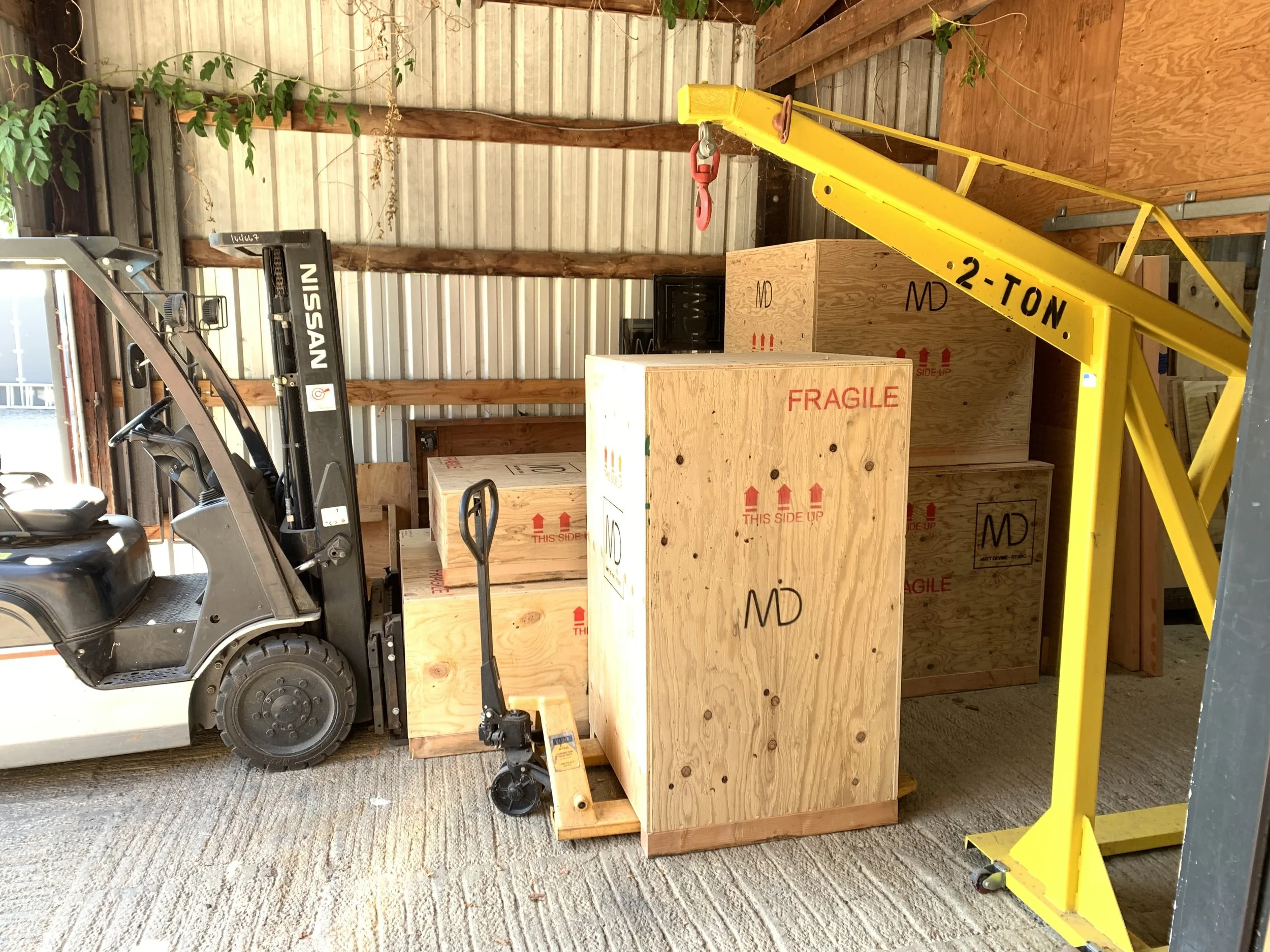 A forklift in a warehouse next to a stack of wooden crates marked with shipping labels and handling instructions, including 'FRAGILE' and 'THIS SIDE UP'.
