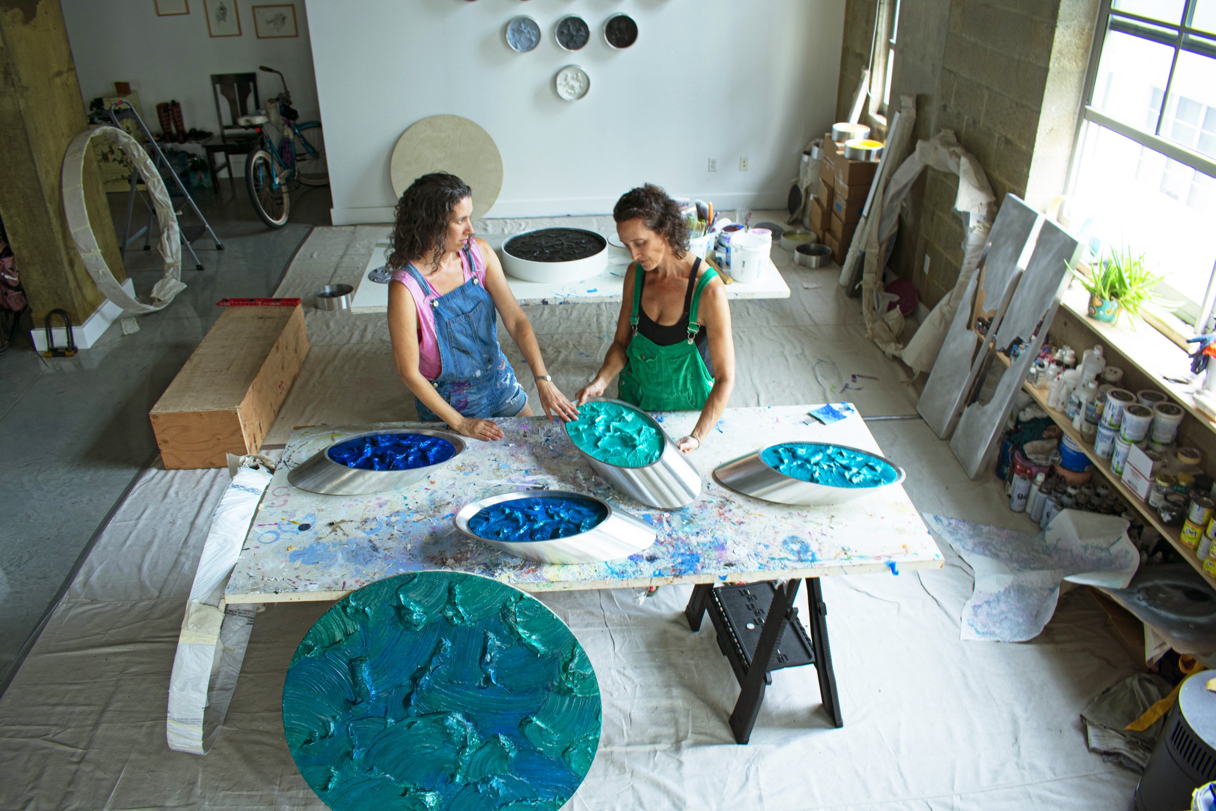 Artists Dana Kleinman and Ruth Avra of KX2 working in their studio with blue pigment, representing artist management and support services offered by Page Art Projects.
