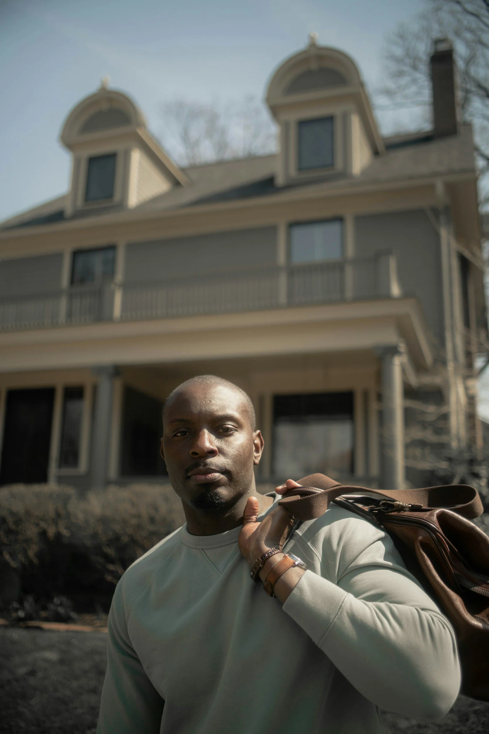 man standing in front of a nice house holding a nice bag financial therapy Colorado Latalia White