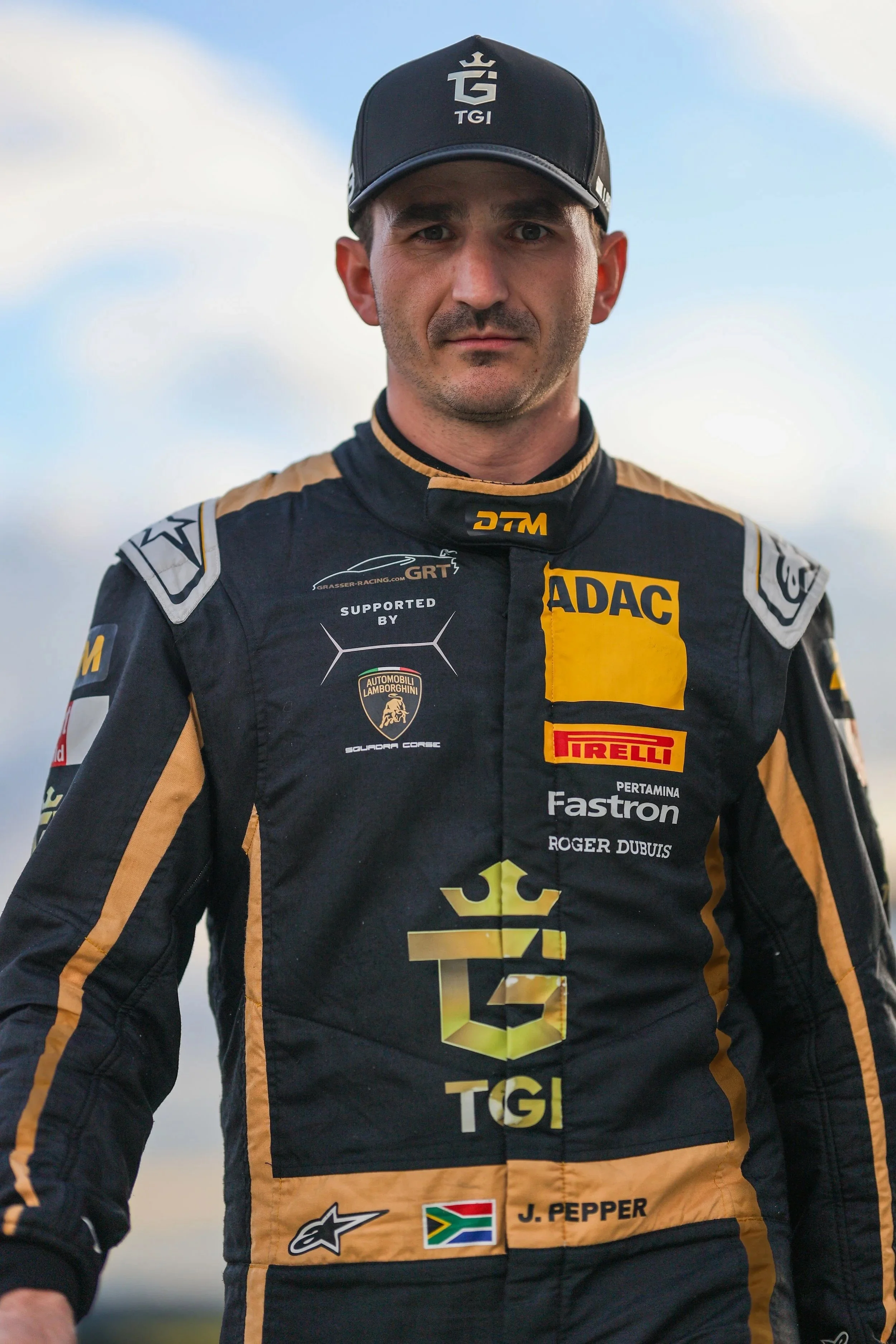 Porträt eines Rennfahrers in schwarzem und goldenem Rennanzug mit Sponsorlogos, trägt eine schwarze Kappe mit Weiß.