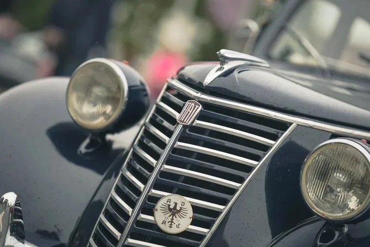 Nahaufnahme des vorderen Bereichs eines schwarzen klassischen Autos mit runden Scheinwerfern, einem verchromten Kühlergrill und einem Fiat-Emblem in der Mitte.