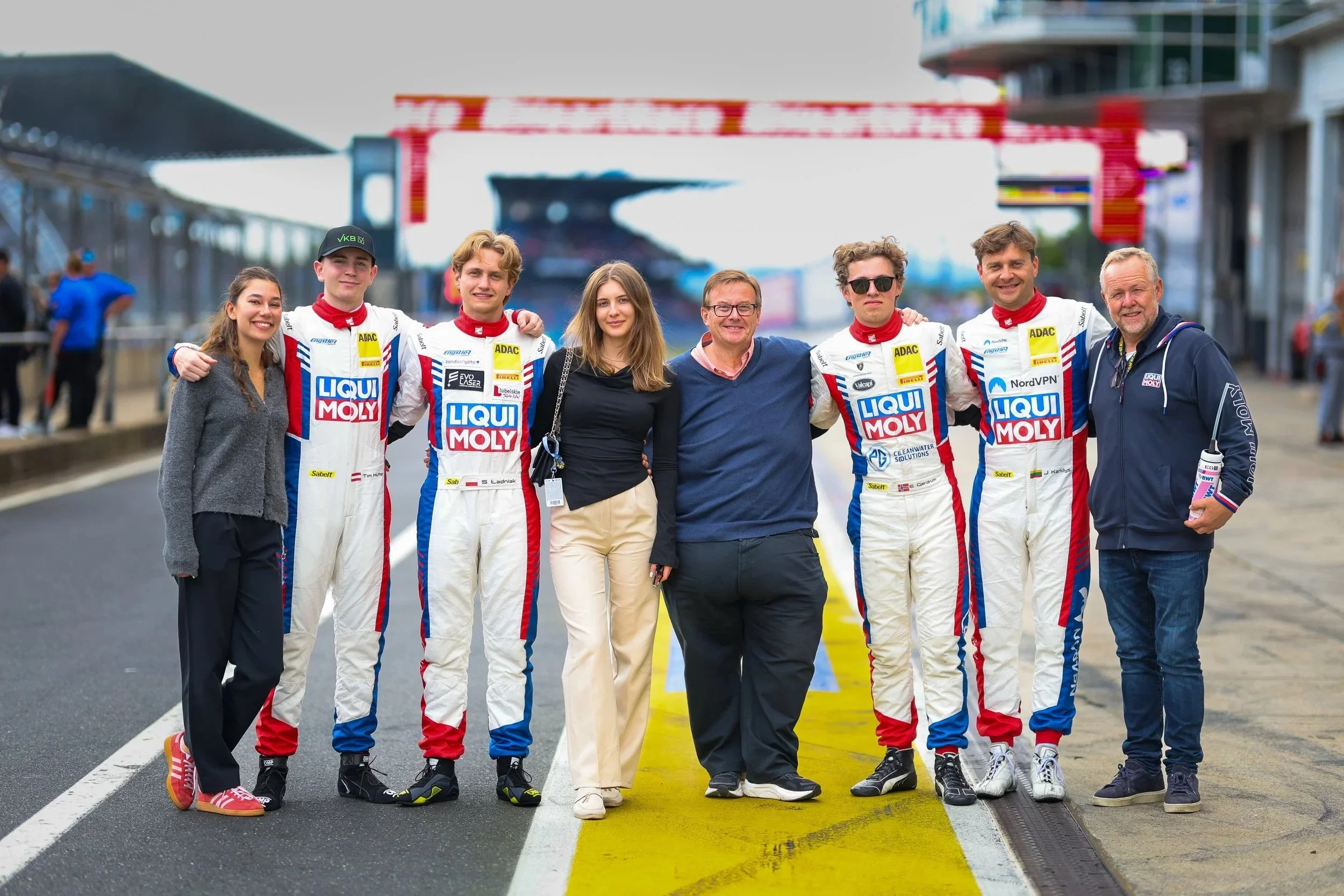 Motorsport-Team nach einem Rennen auf der Rennstrecke, alle sind lächelnd und posieren für das Foto.