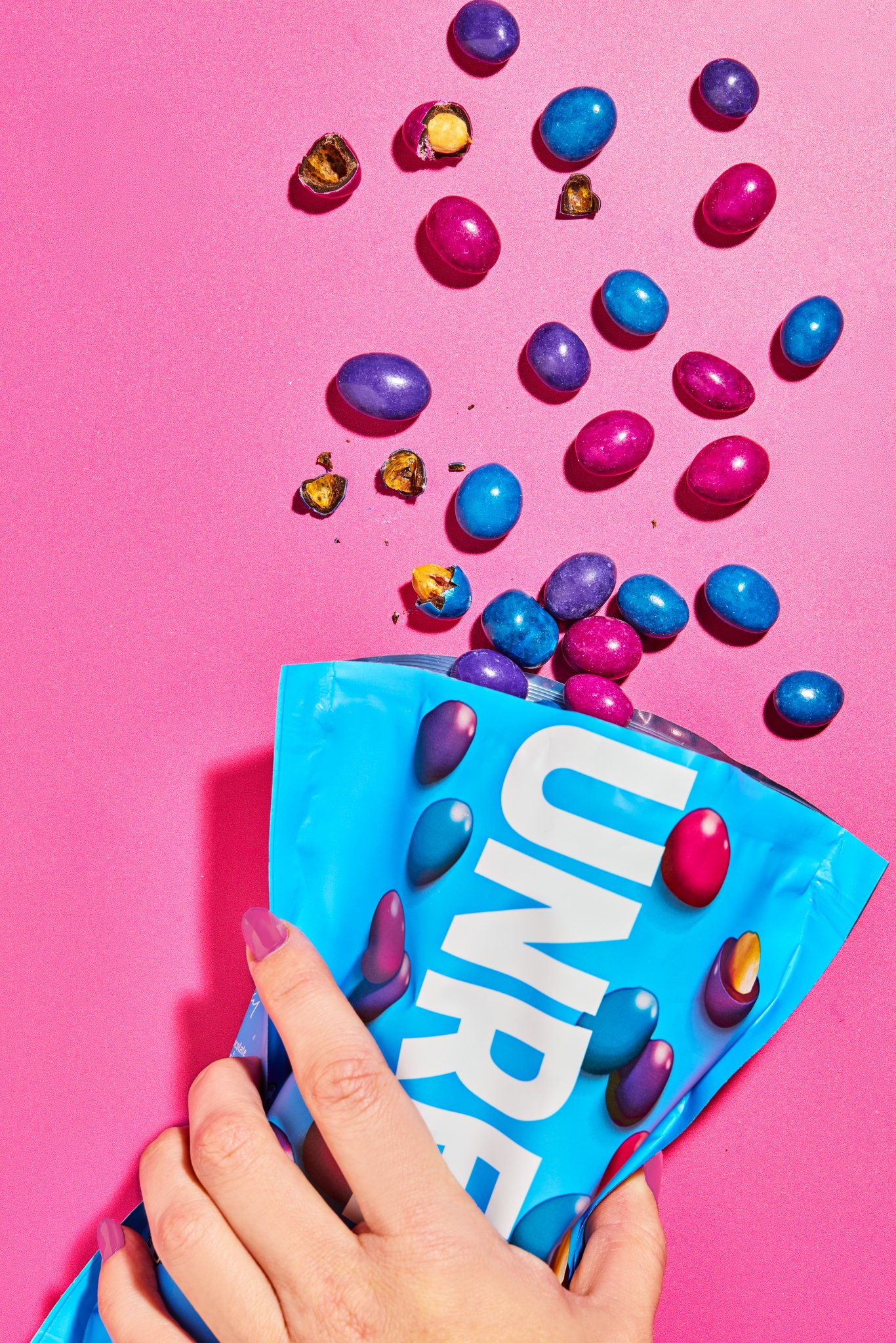 Colorful candy eggs spilling from a blue and white package onto a pink background.