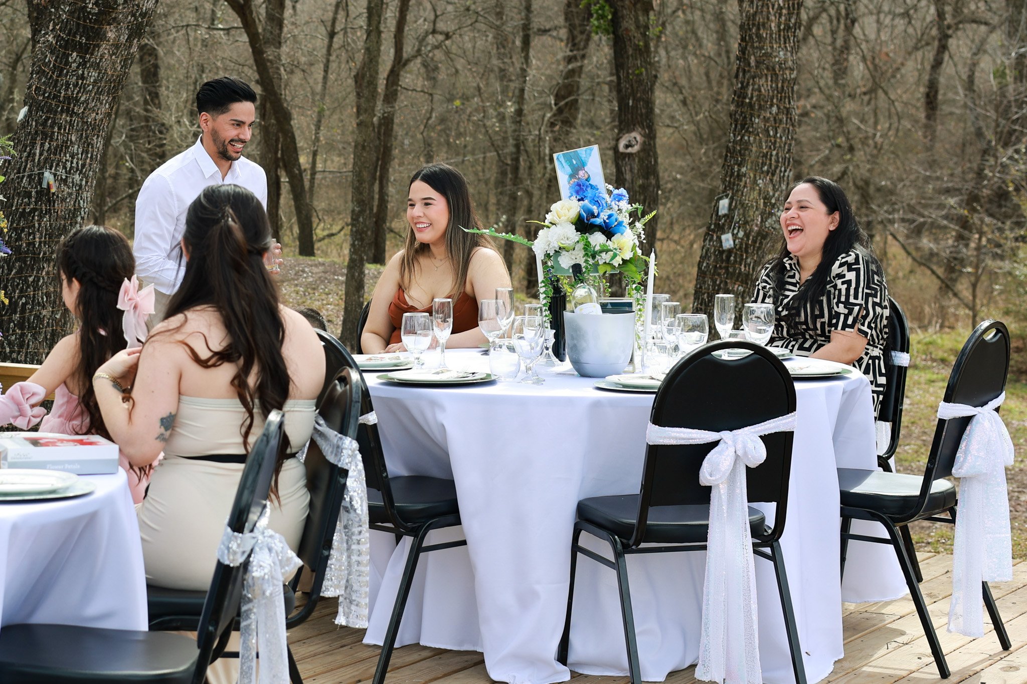 People celebrating at an outdoor event with a decorated table, trees in the background, and smiling guests.