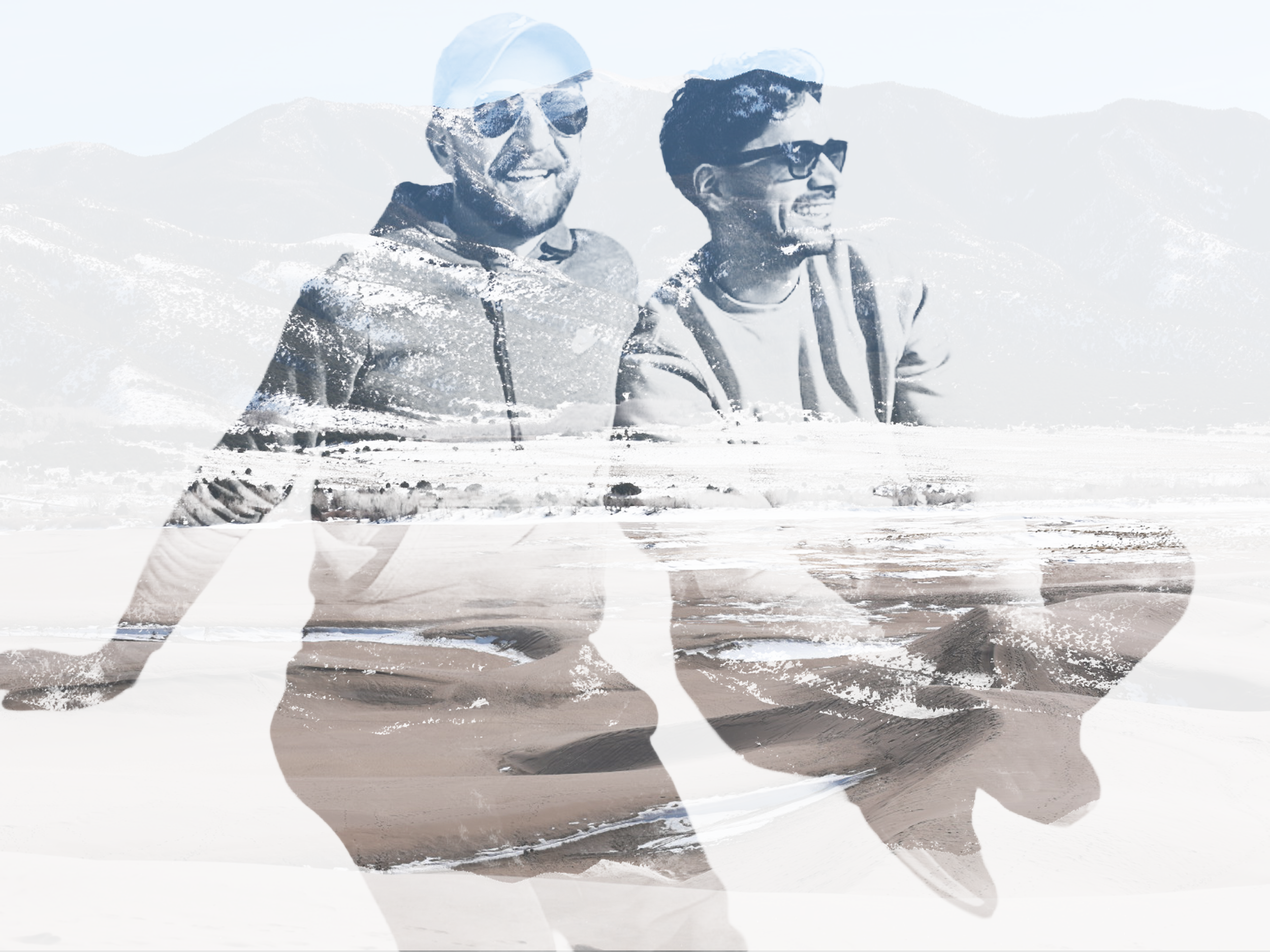 Double exposure image of two men in sunglasses and casual clothing, smiling and looking into the distance, with a mountain range and desert landscape in the background.