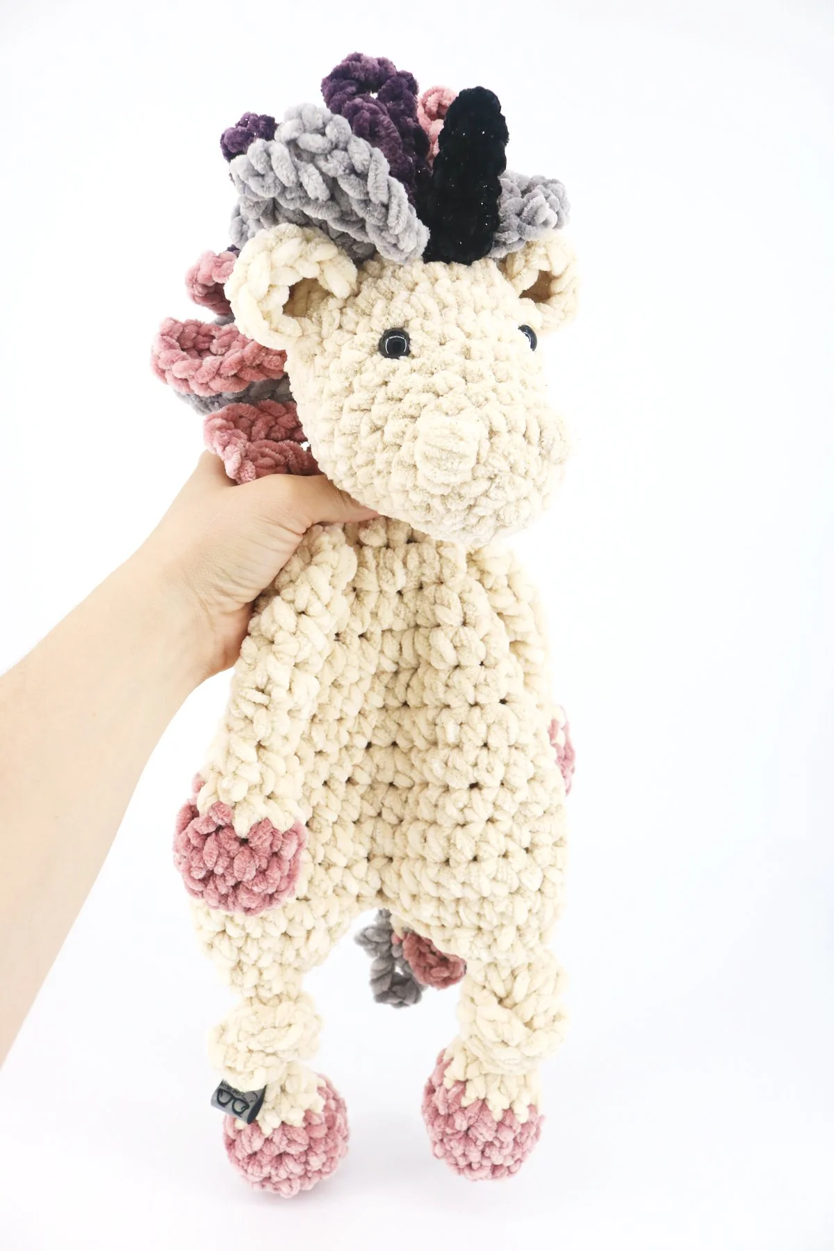 A velvet unicorn lovey is being held up by the back of it's shoulders