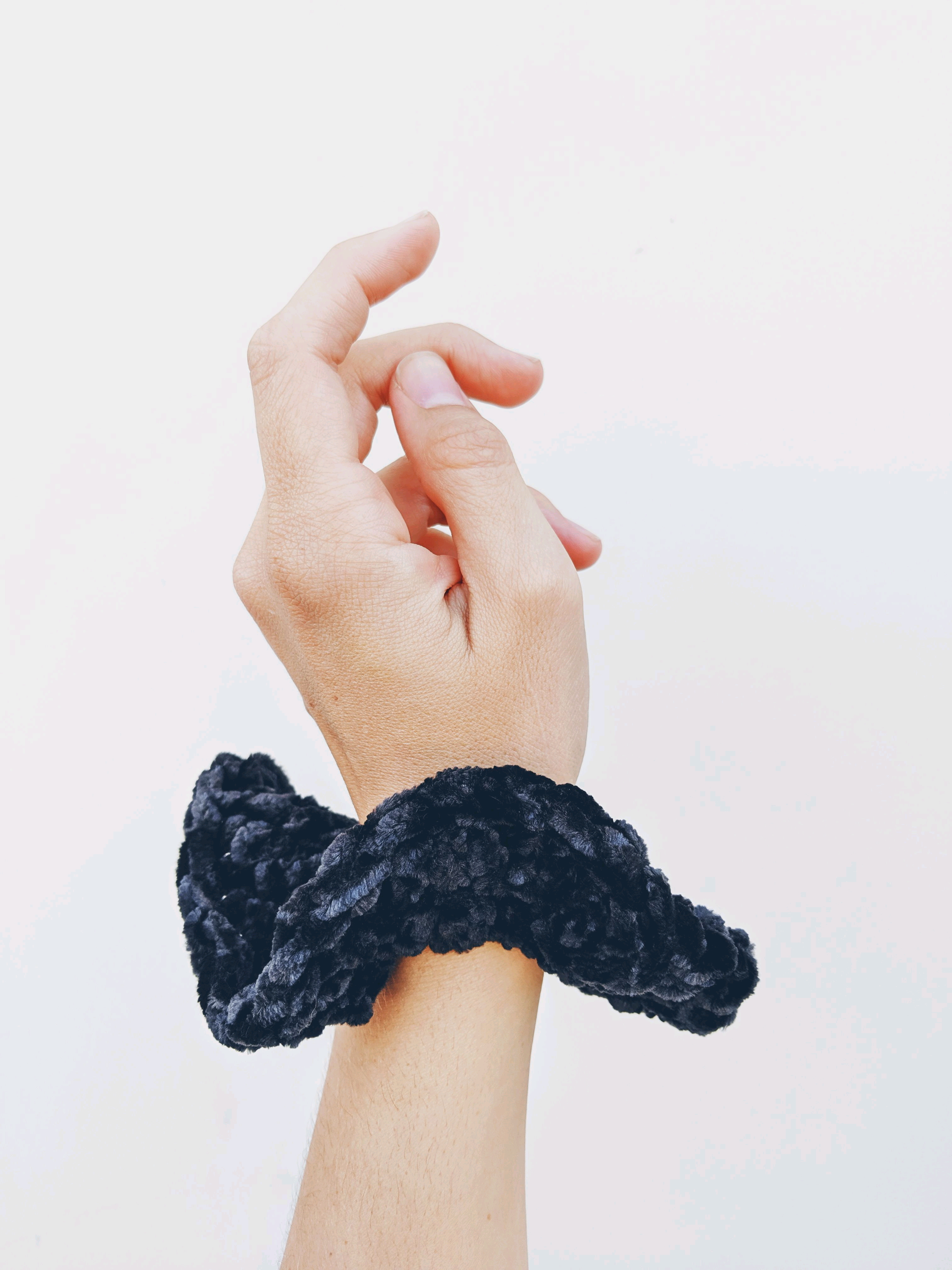 a black scrunchie adorns a wrist with a white backgound