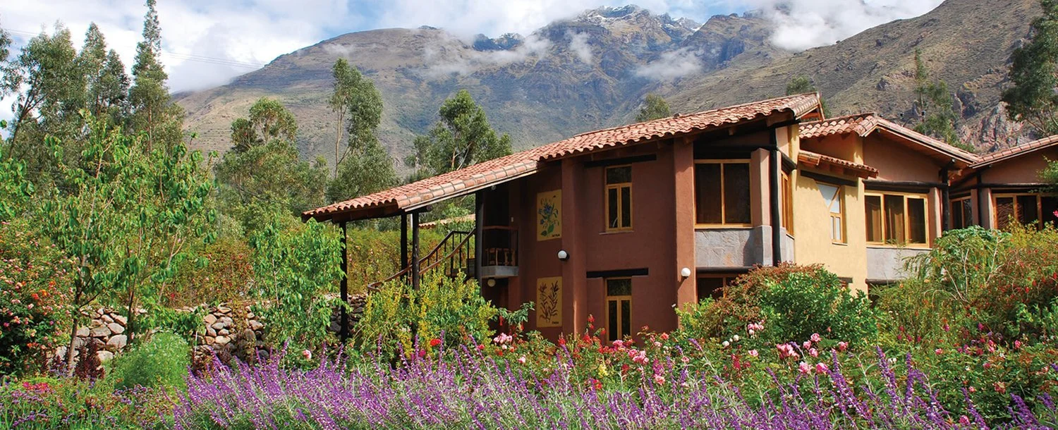A house surrounded by colorful flowers and greenery with mountains in the background.