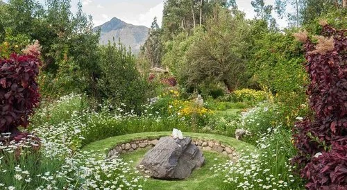 A lush garden with various trees and shrubs, a large rock in the center surrounded by a circular stone border, and mountains in the background.