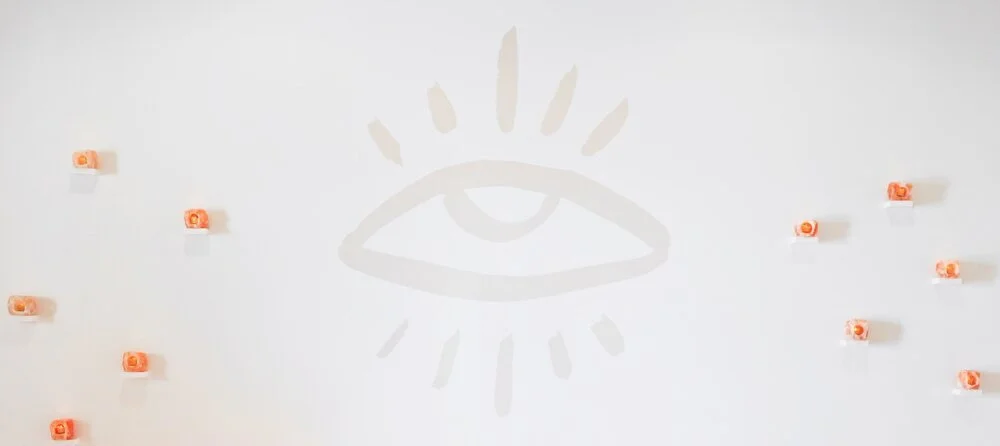 Wall mural with eye illustration and small orange and white objects arranged around it.