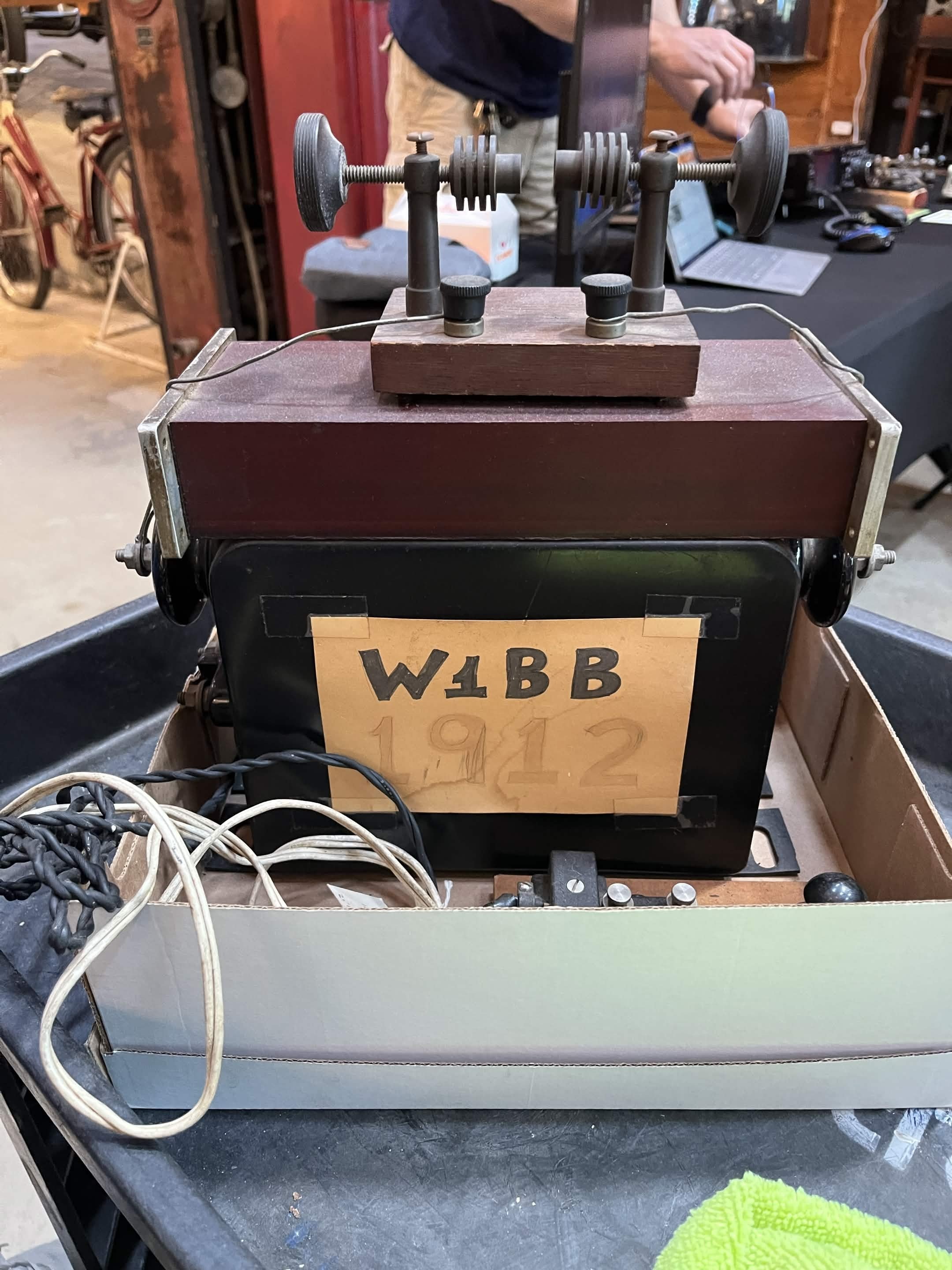 Vintage electrical testing device with dials and knobs on wooden base, with cords connected, set on a black workbench with a green towel nearby.