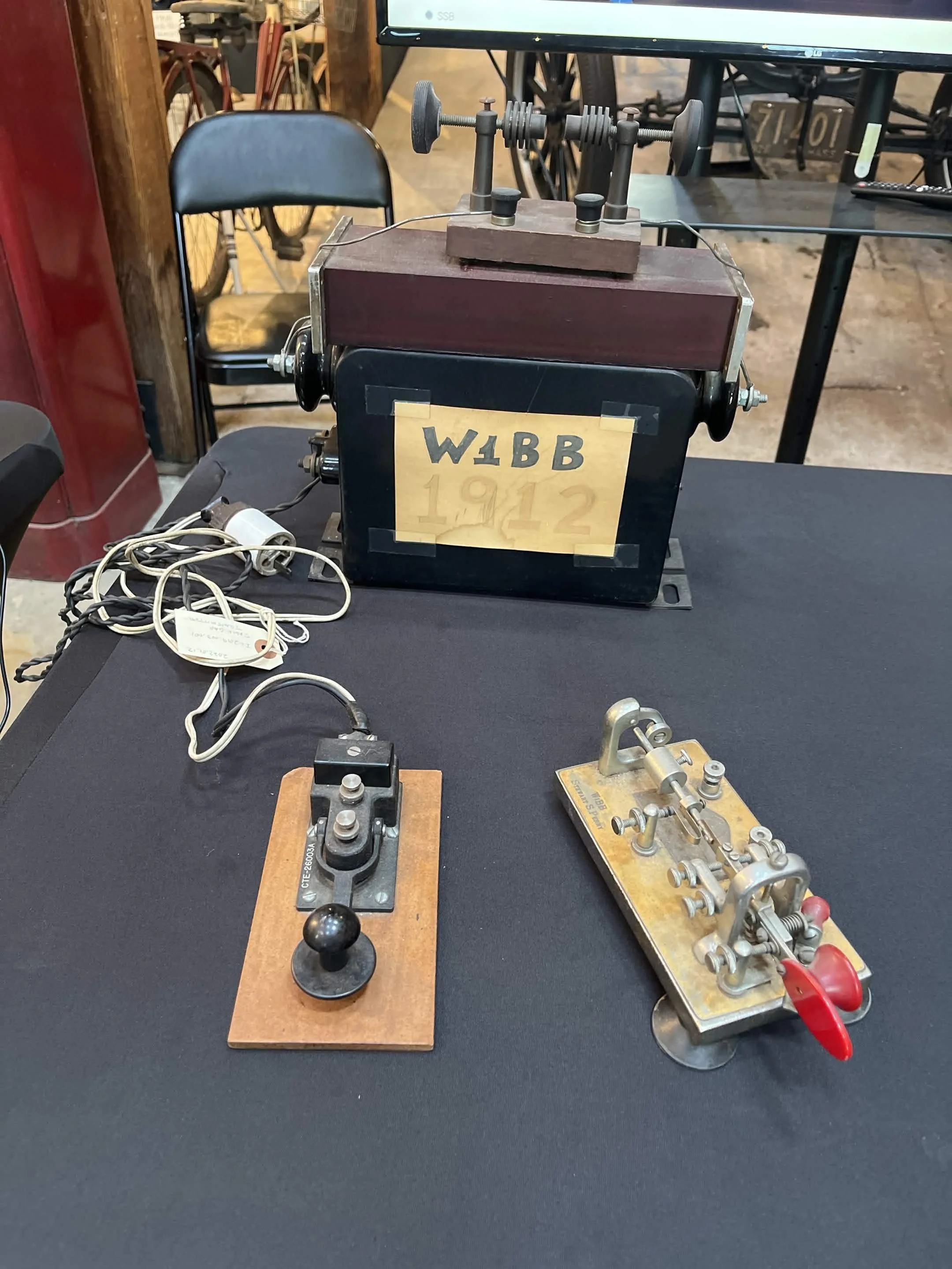 An antique telegraph machine with a hand crank, a key, and a relay setup on a black table at a vintage technology exhibit.