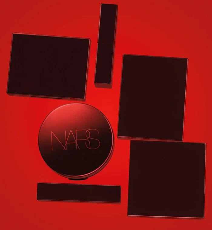 A collection of black NARS makeup products, including a compact, a lipstick, and various square cases, arranged on a red background.