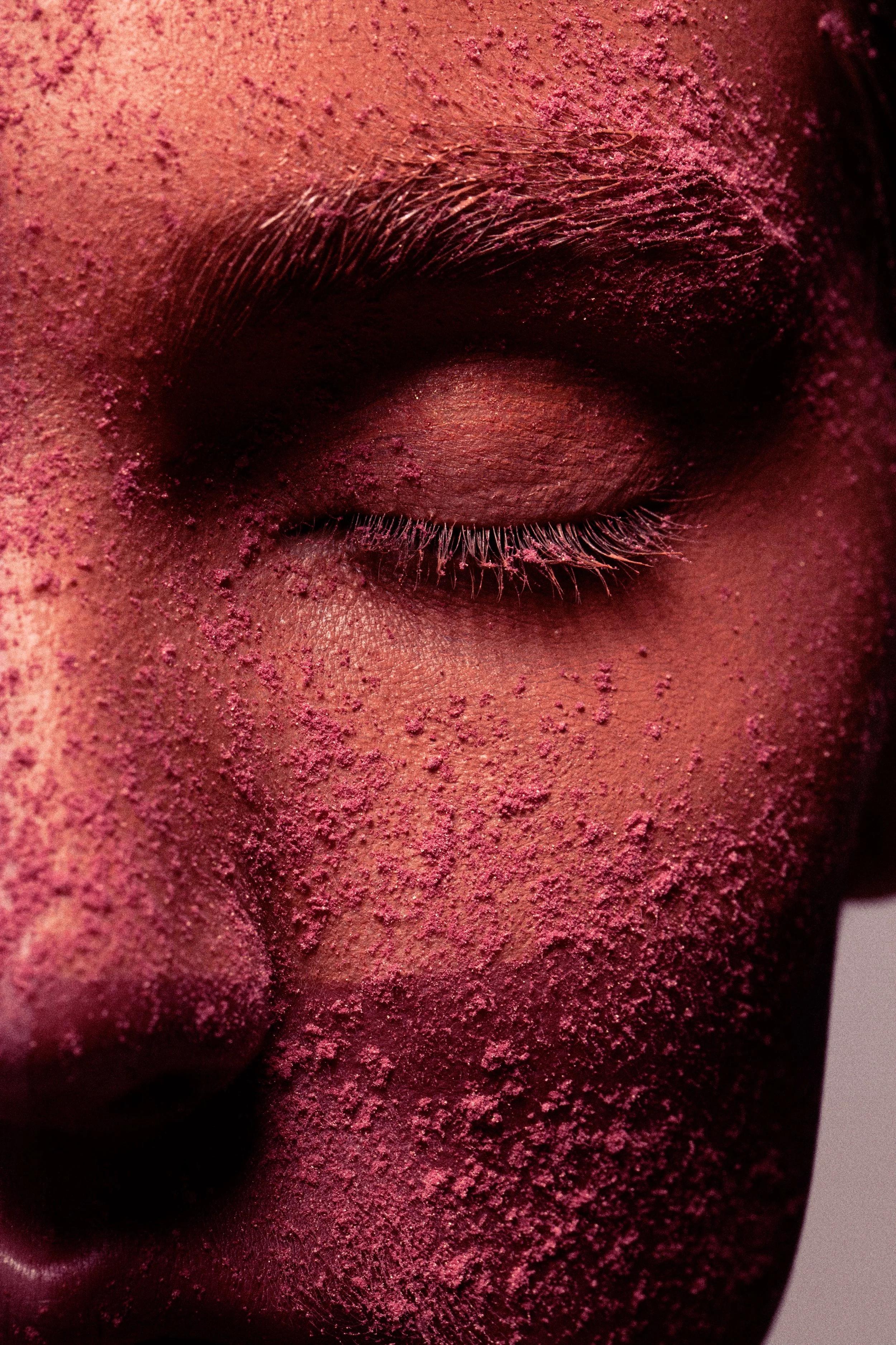 Close-up of a person's face with closed eye, covered in pink powder.