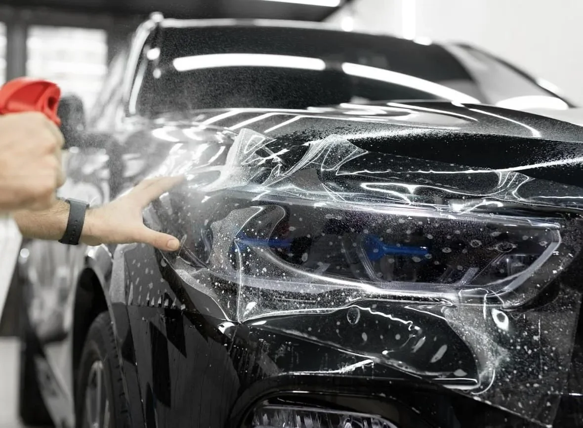 Person cleaning or inspecting the front headlight of a black car in an indoor garage