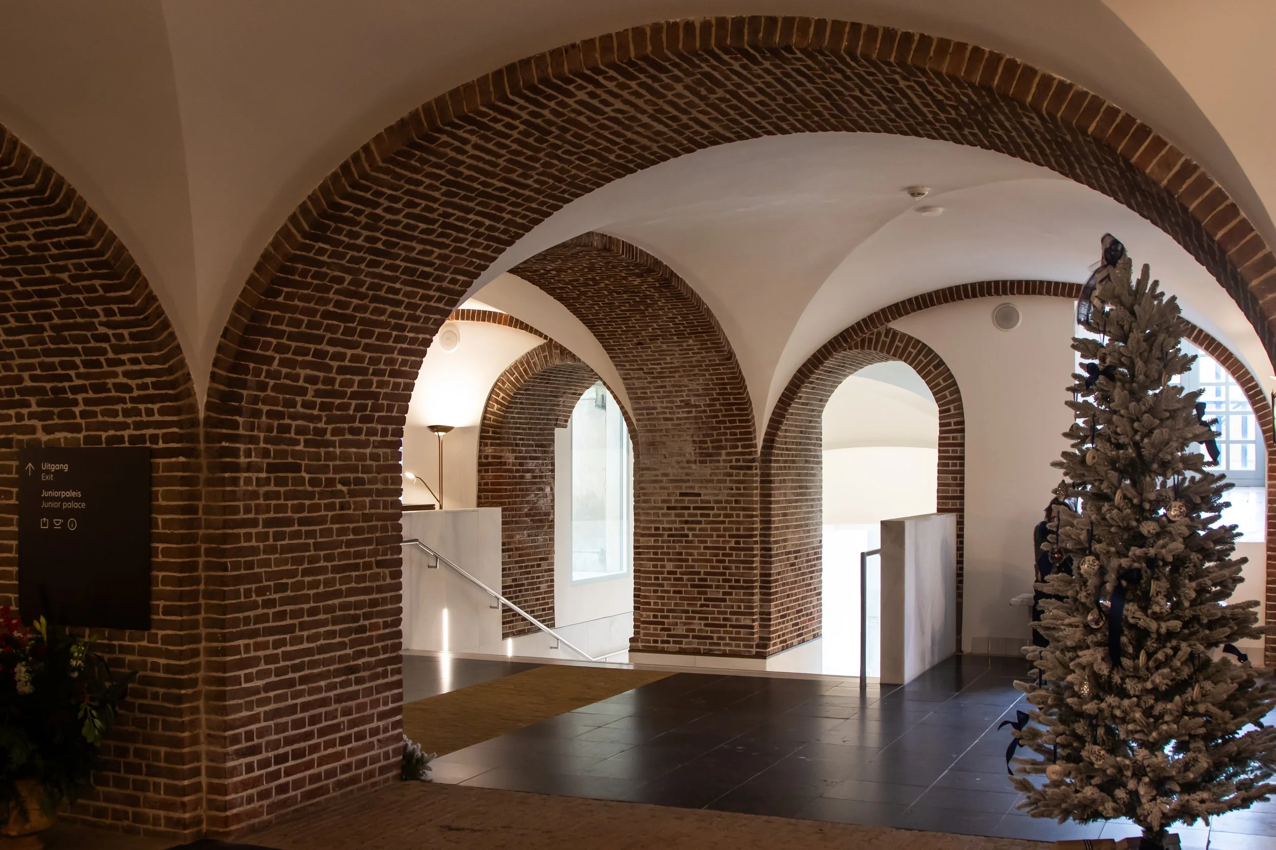 Interieur van een gebouw met bakstenen bogen, een kerstboom met decoraties en zachte verlichting.