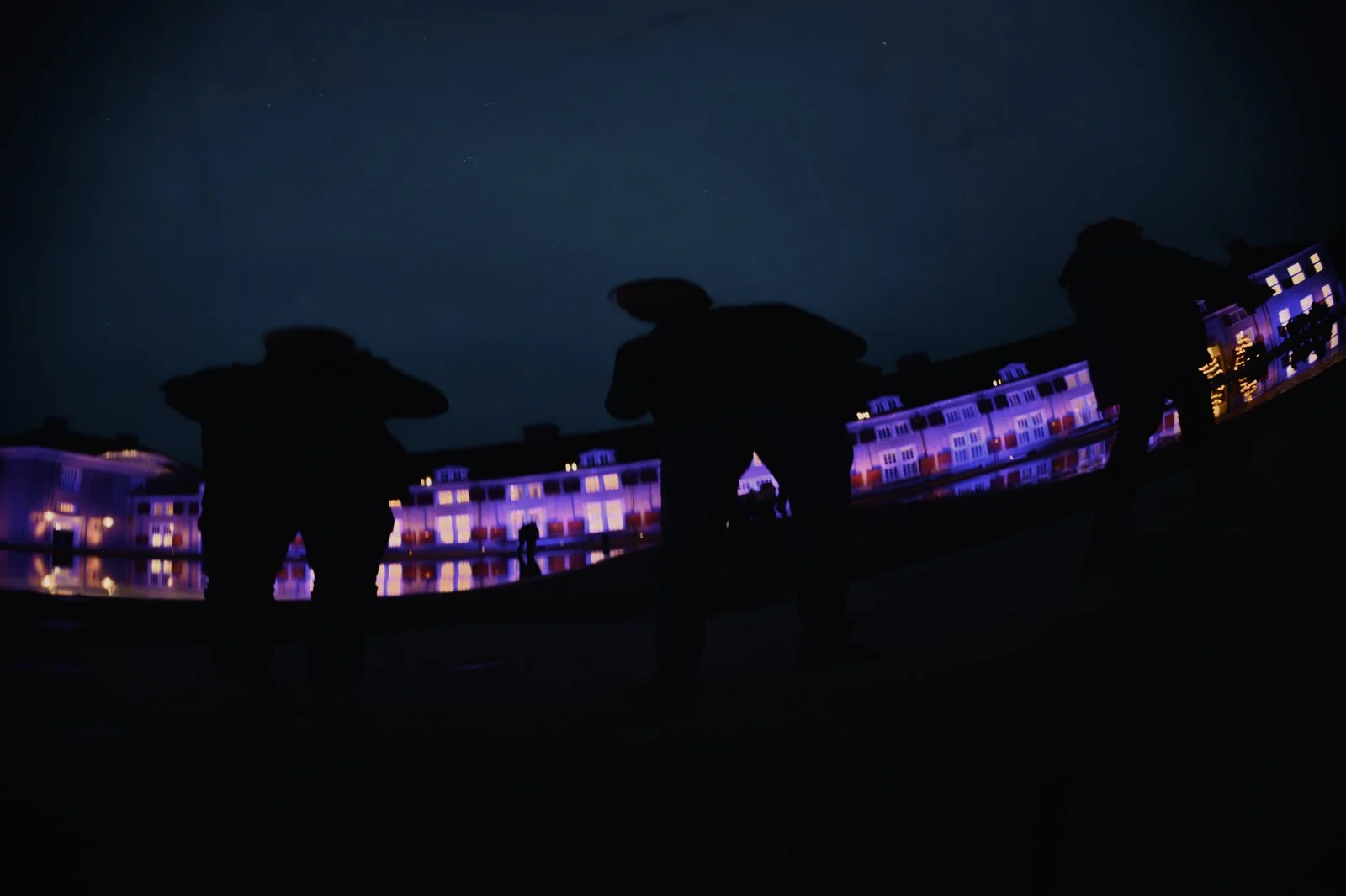 Silhouetten van mensen bij nacht met verlichte gebouwen op de achtergrond.
