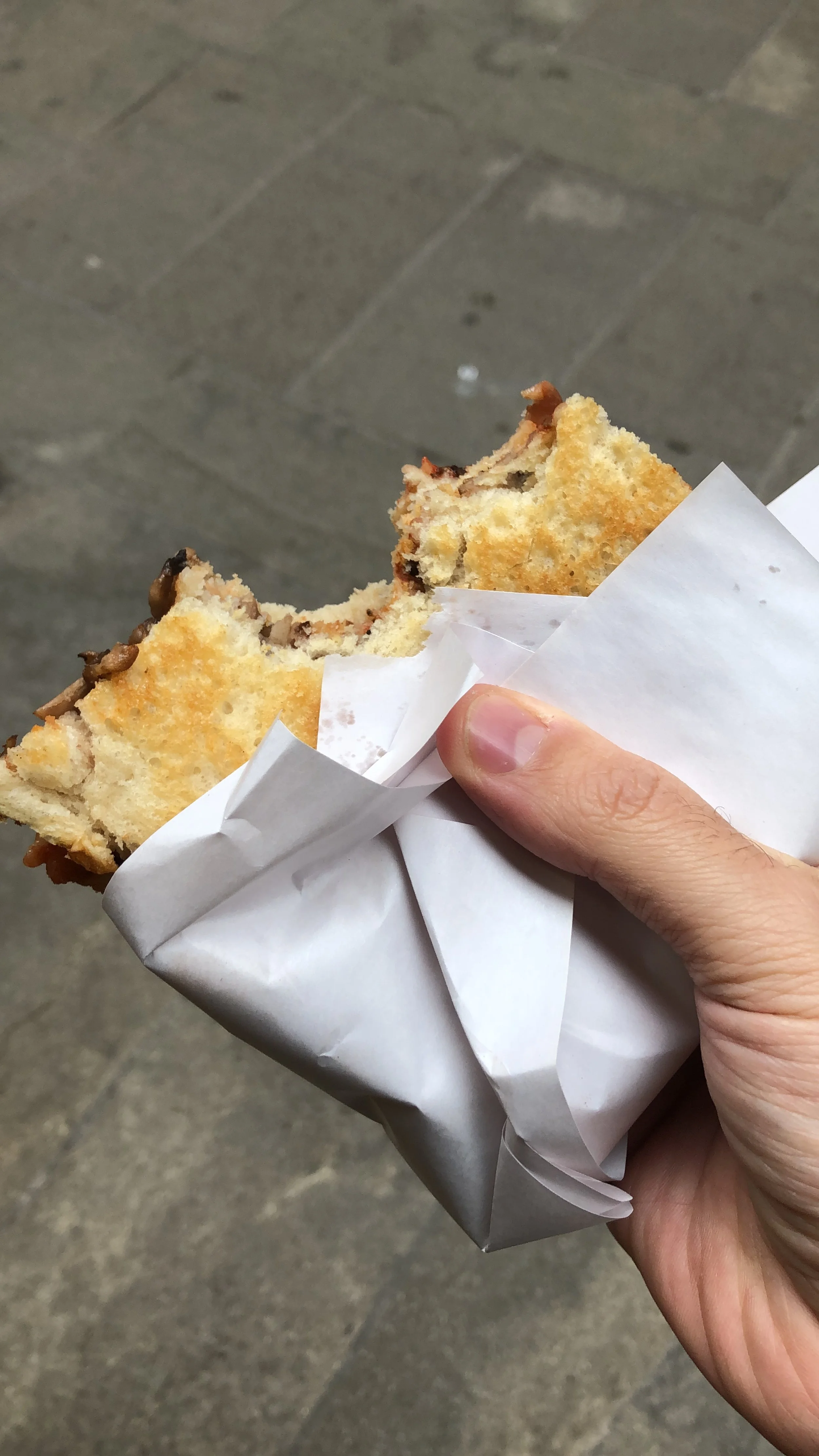 Mano che tiene un panino avvolto in carta bianca, con un morso.